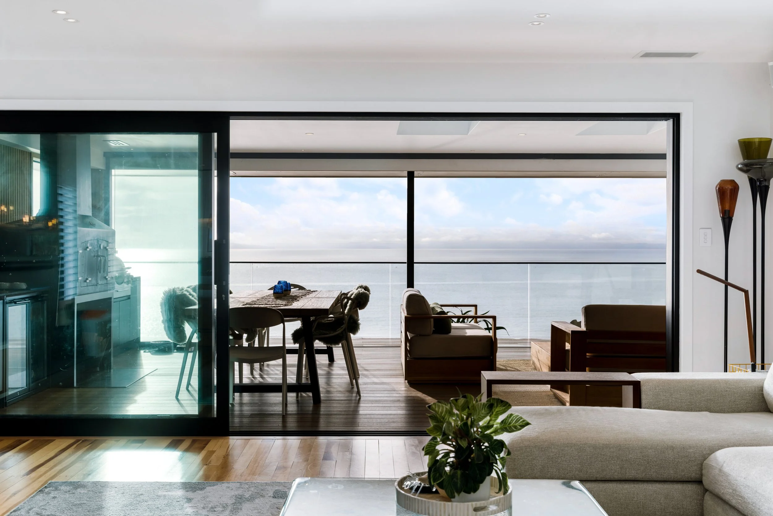 Living room with large glass door leading to a balcony with ocean view, modern furniture, and decorative vases.
