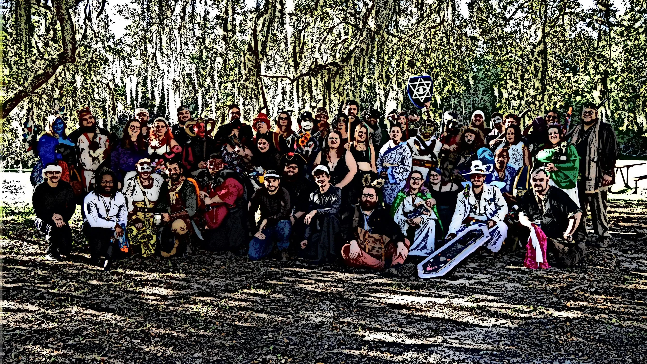 Group of people dressed in colorful costumes and masks, gathered outdoors in a forested area.
