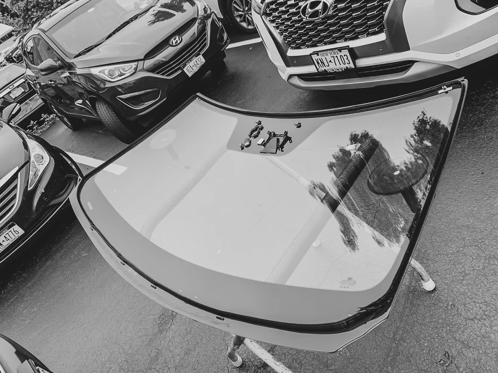 Black and white photo of a replacement windshield resting on a stand outdoors