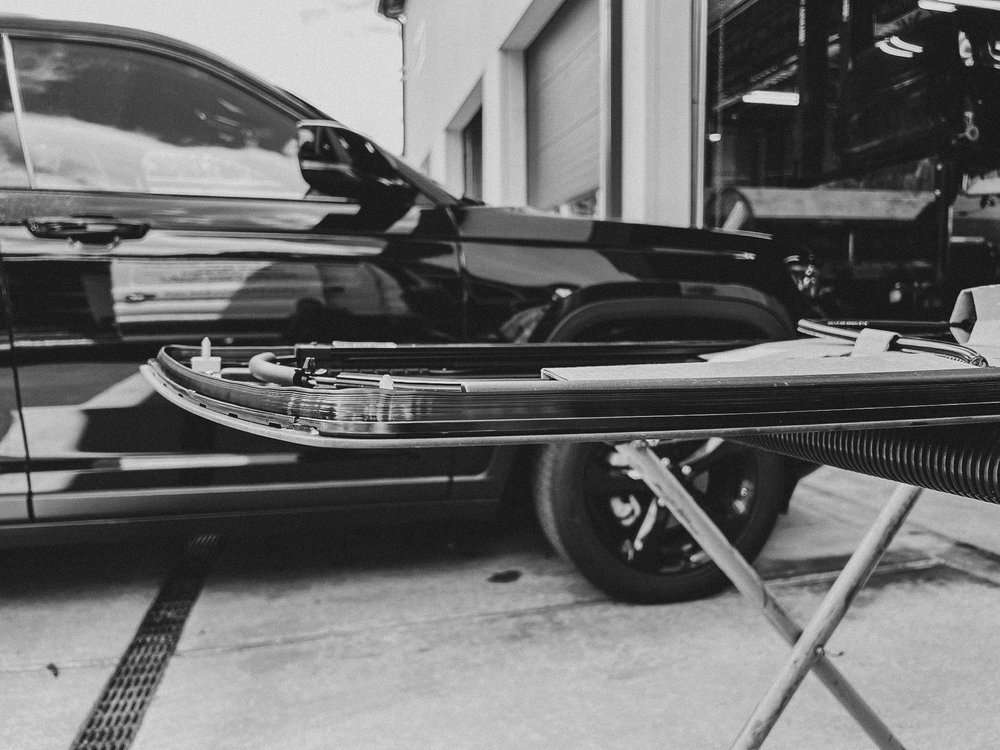 Black and white image of a car windshield being replaced outside the garage