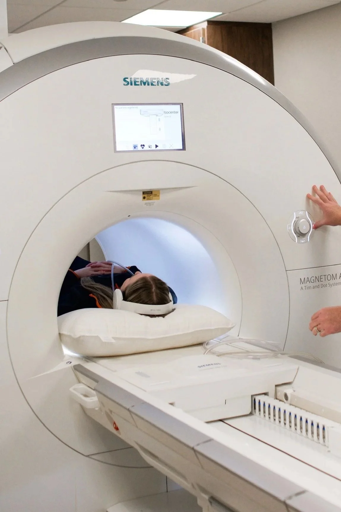 A woman lying on a pillow inside a medical MRI machine with a healthcare professional standing beside it, preparing for the scan.