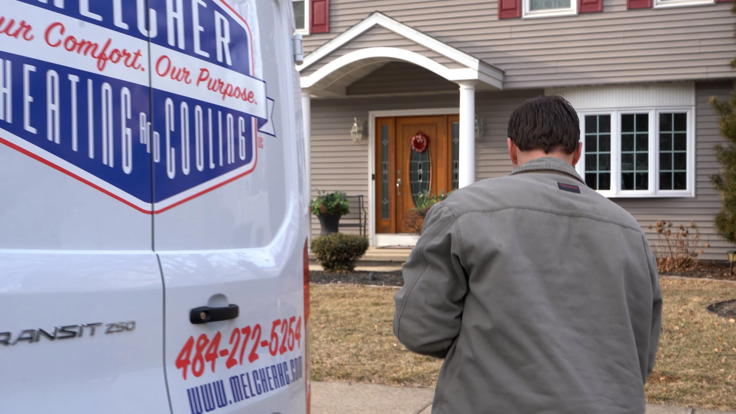 Front of a residential house with a man walking towards the door, and a white service van parked in front with company info.
