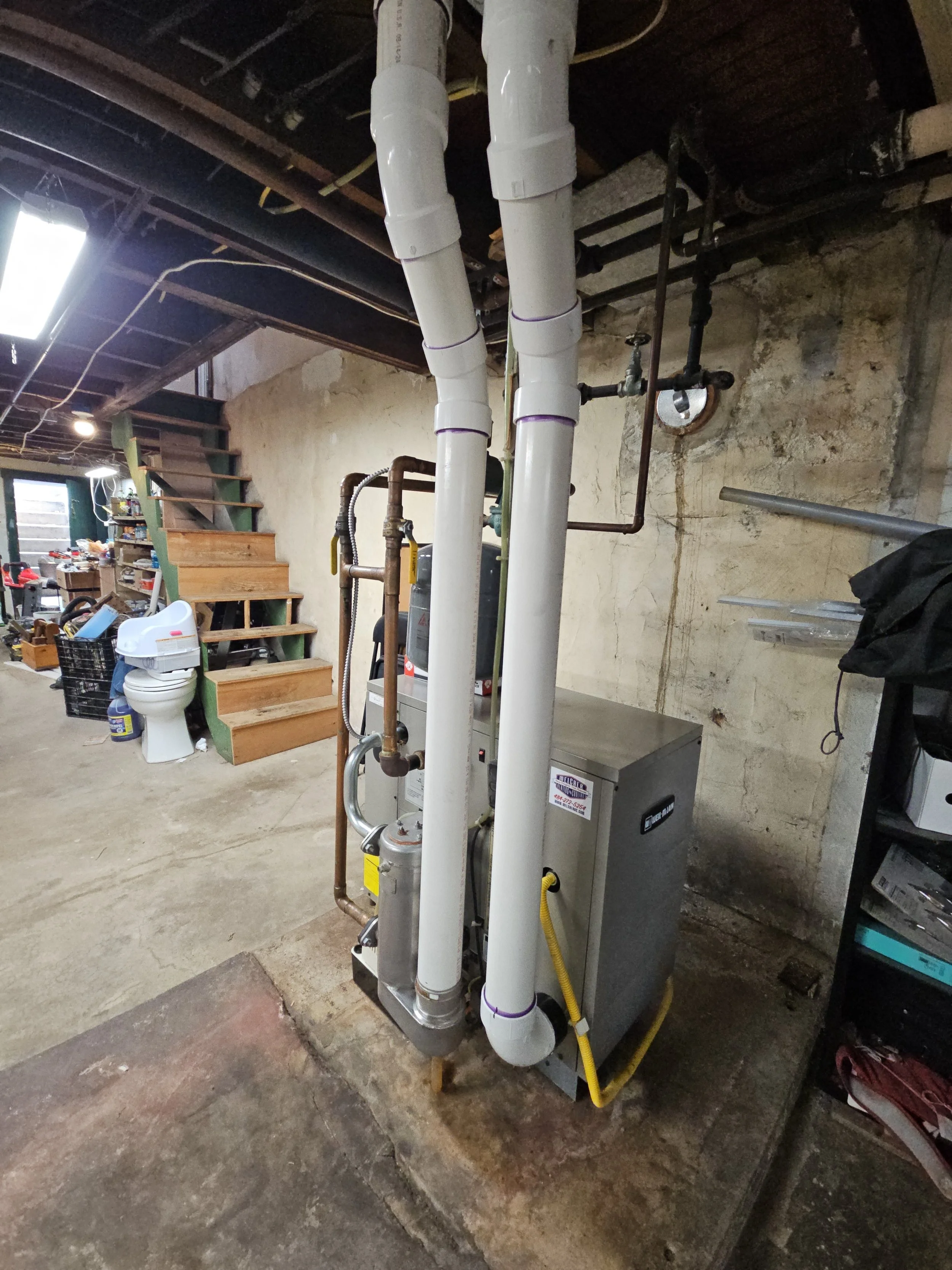 Basement with plumbing pipes and utility equipment, including a water heater, stairs, and various tools and storage items.