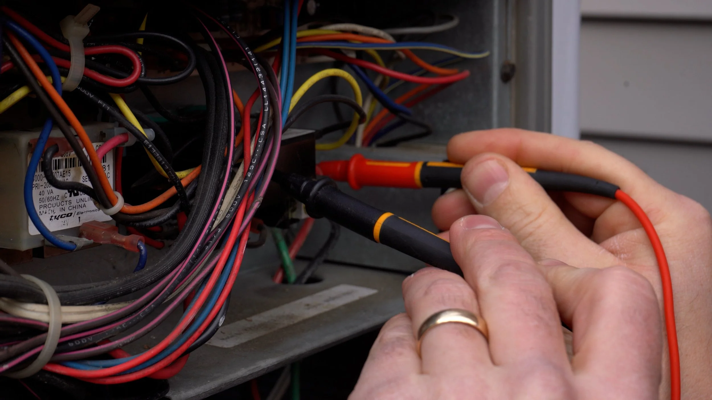 A person using a screwdriver to work on the wiring inside an electrical panel, with various colored wires and a label visible.