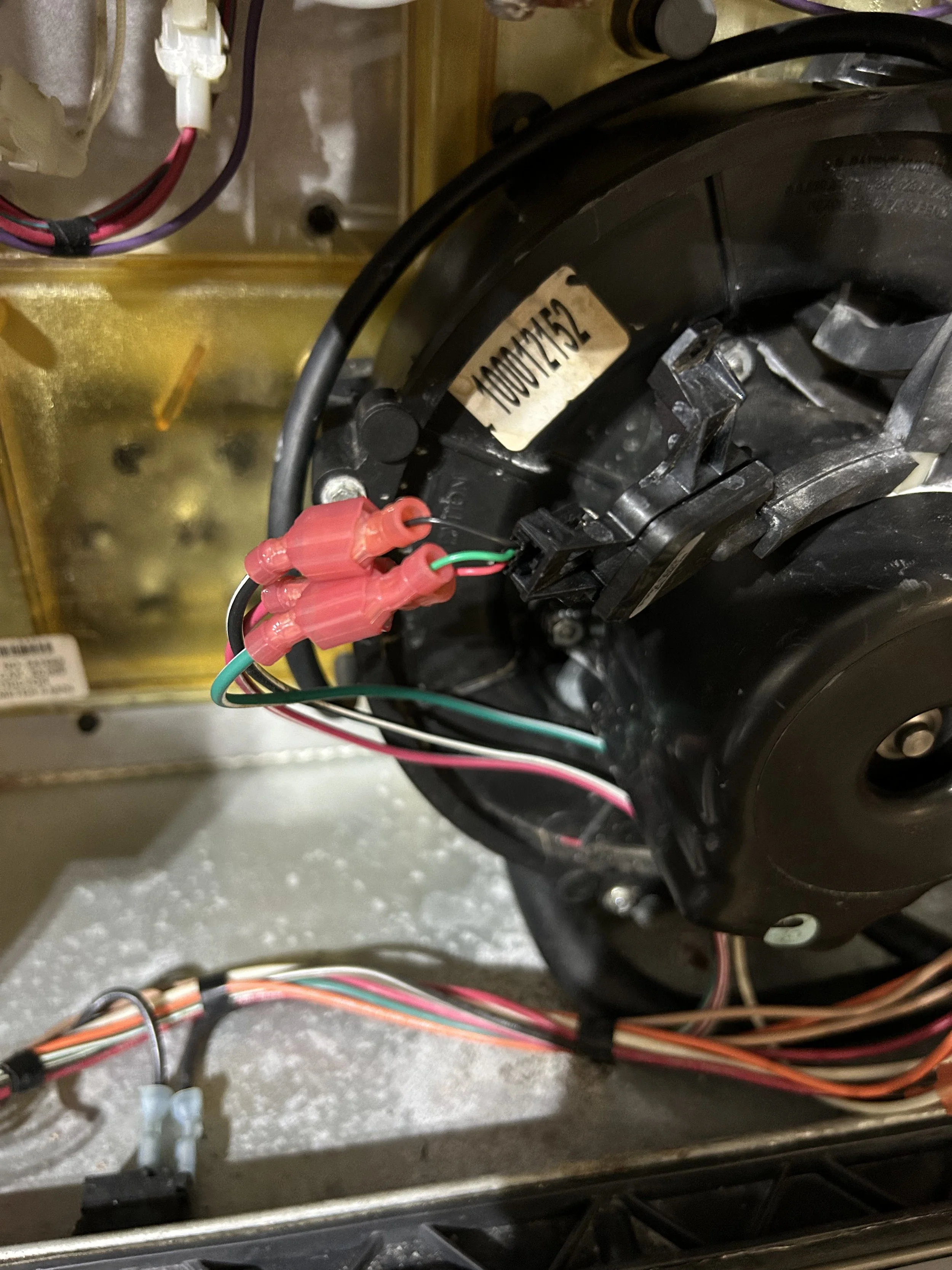 Close-up of electrical wiring and components inside a machine or appliance, including wires connected with red and green connectors, a black circular component, and a yellow metallic surface in the background.
