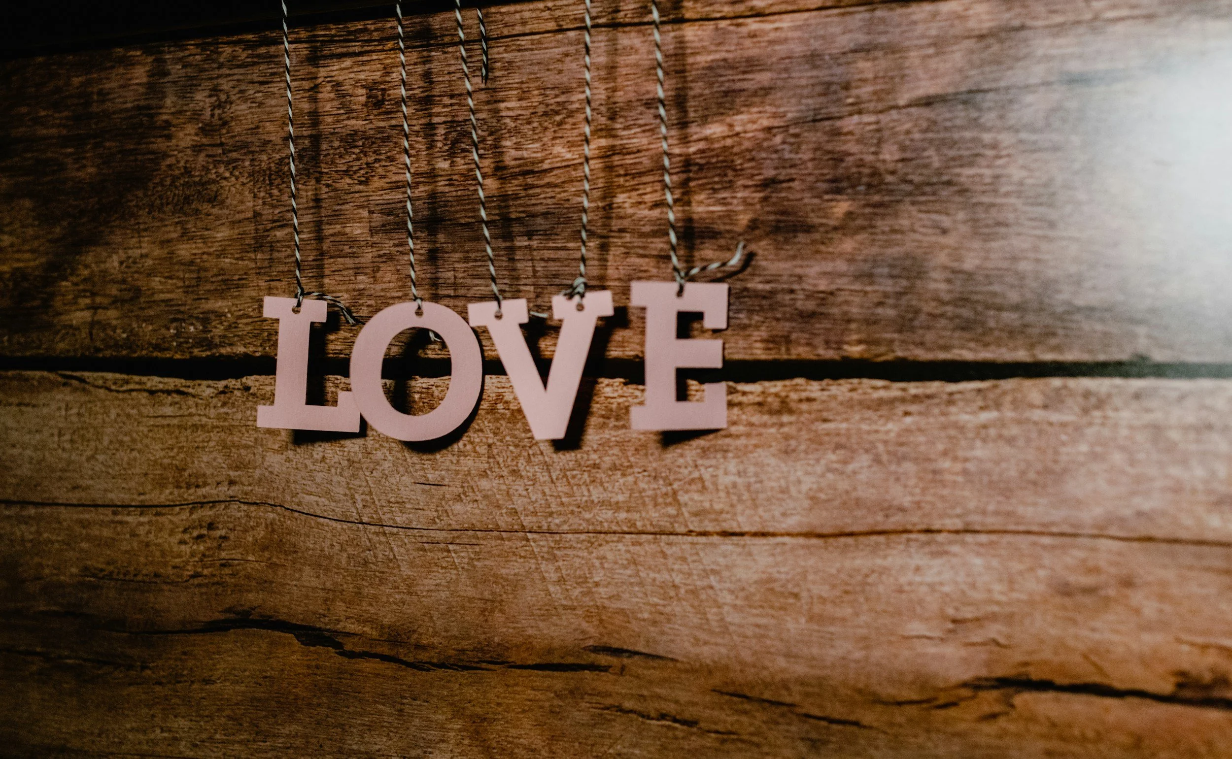 Pink decorative letters spelling "LOVE" hanging from black and white twine on a wooden wall.
