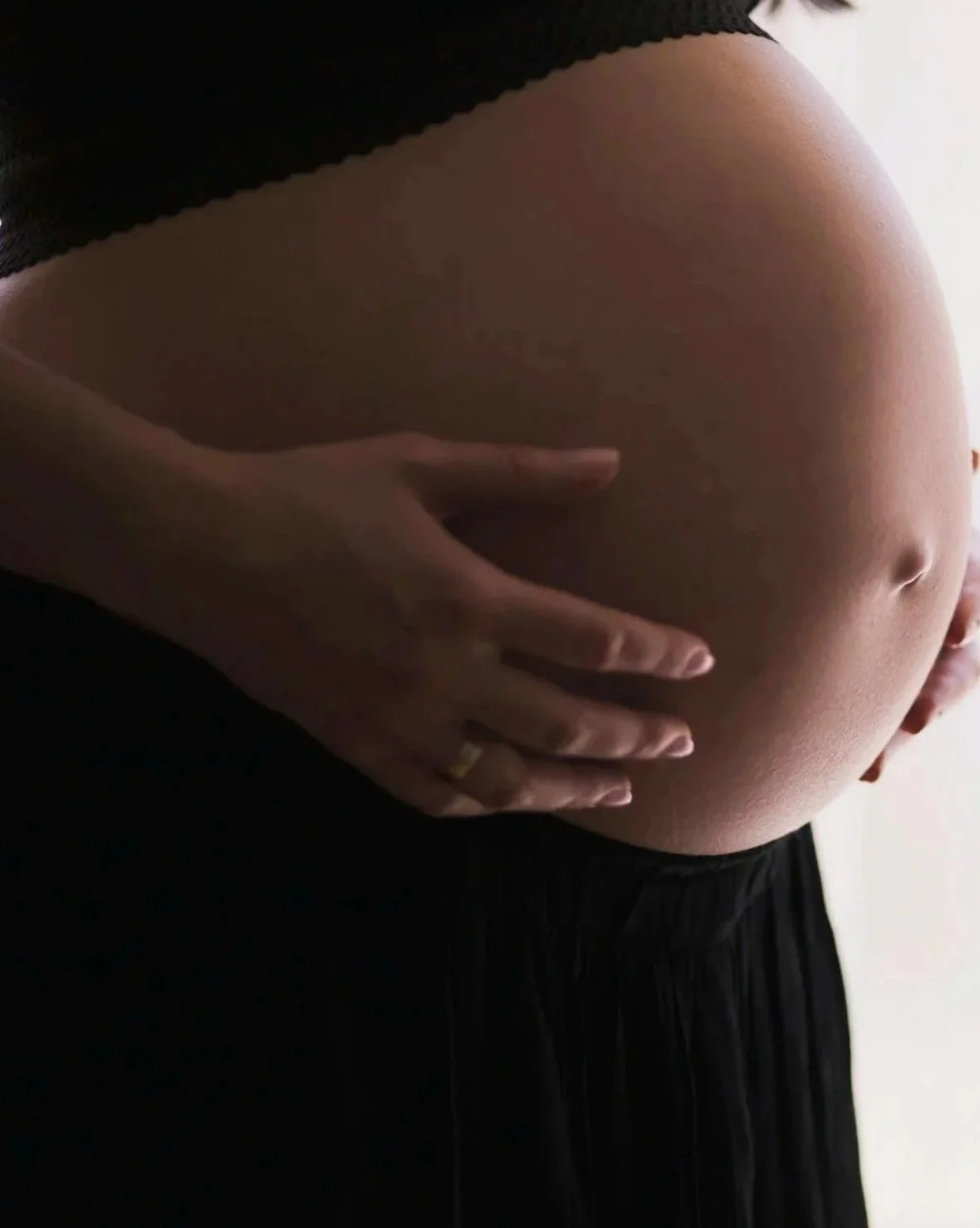 Pregnant woman holding her belly, representing pregnancy and maternal wellbeing.