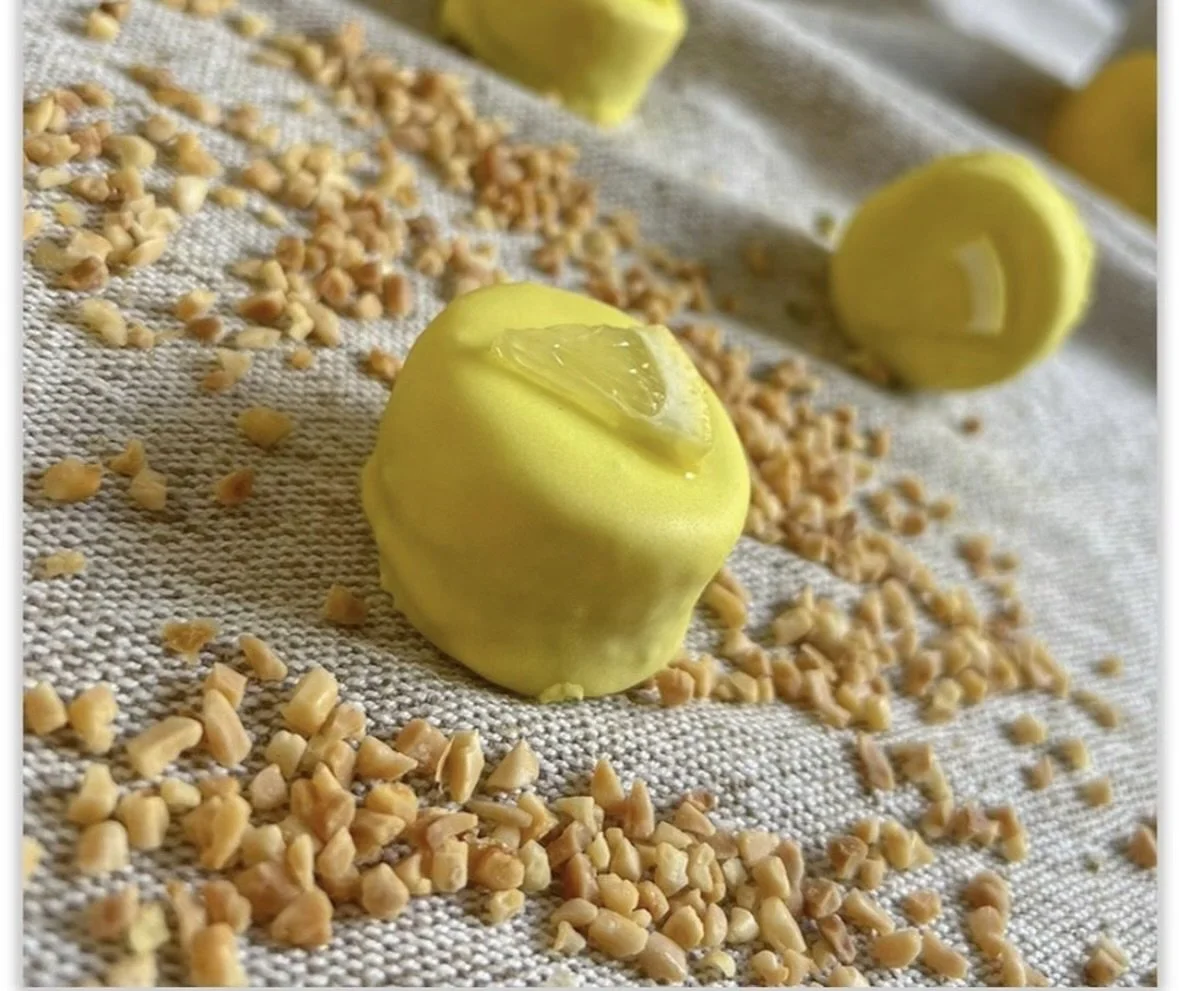 Yellow candy apple with lemon slice decoration on top, surrounded by chopped nuts on a textured surface.