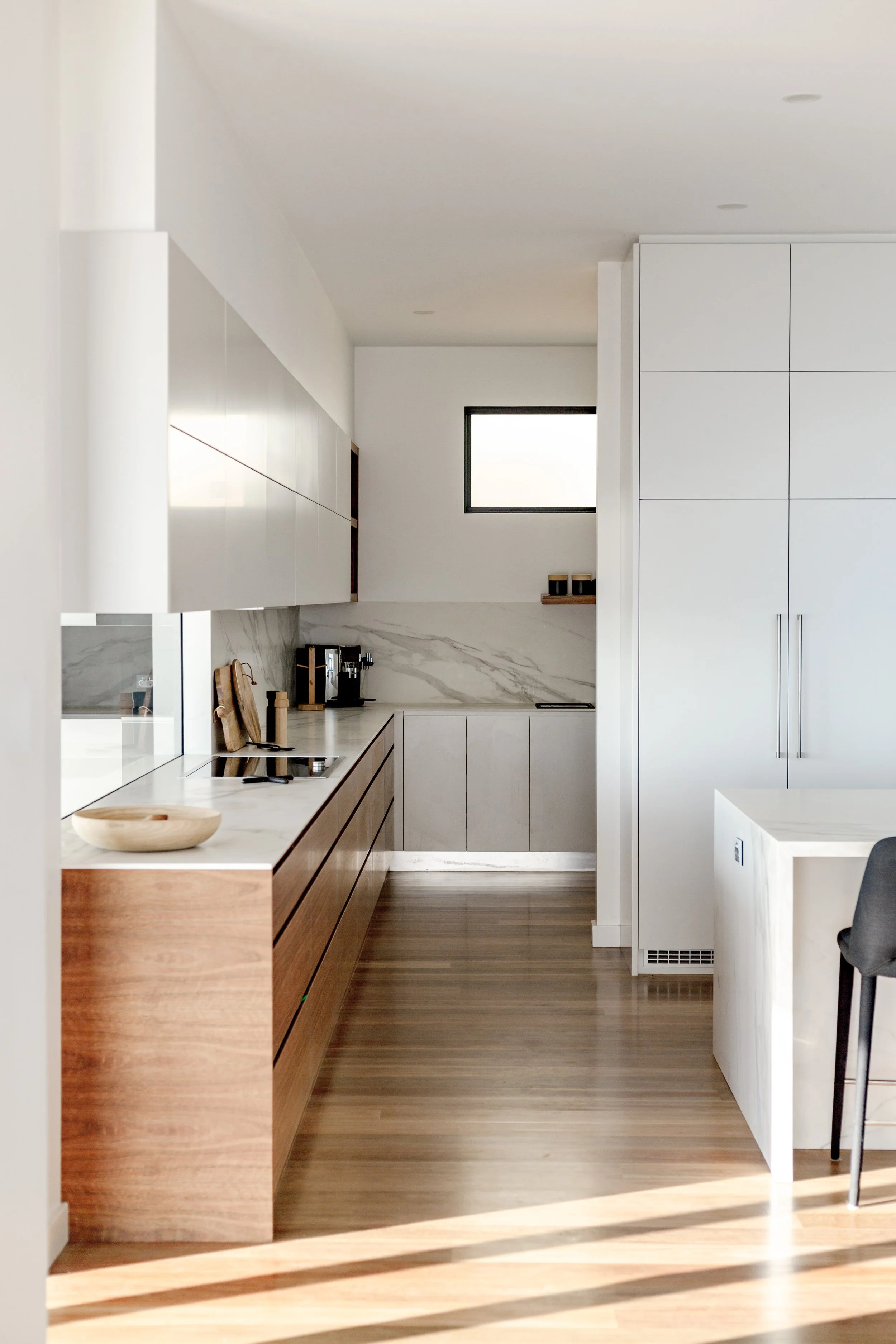 Modern kitchen with white upper cabinets, wooden lower cabinets, a marble backsplash, and a small window