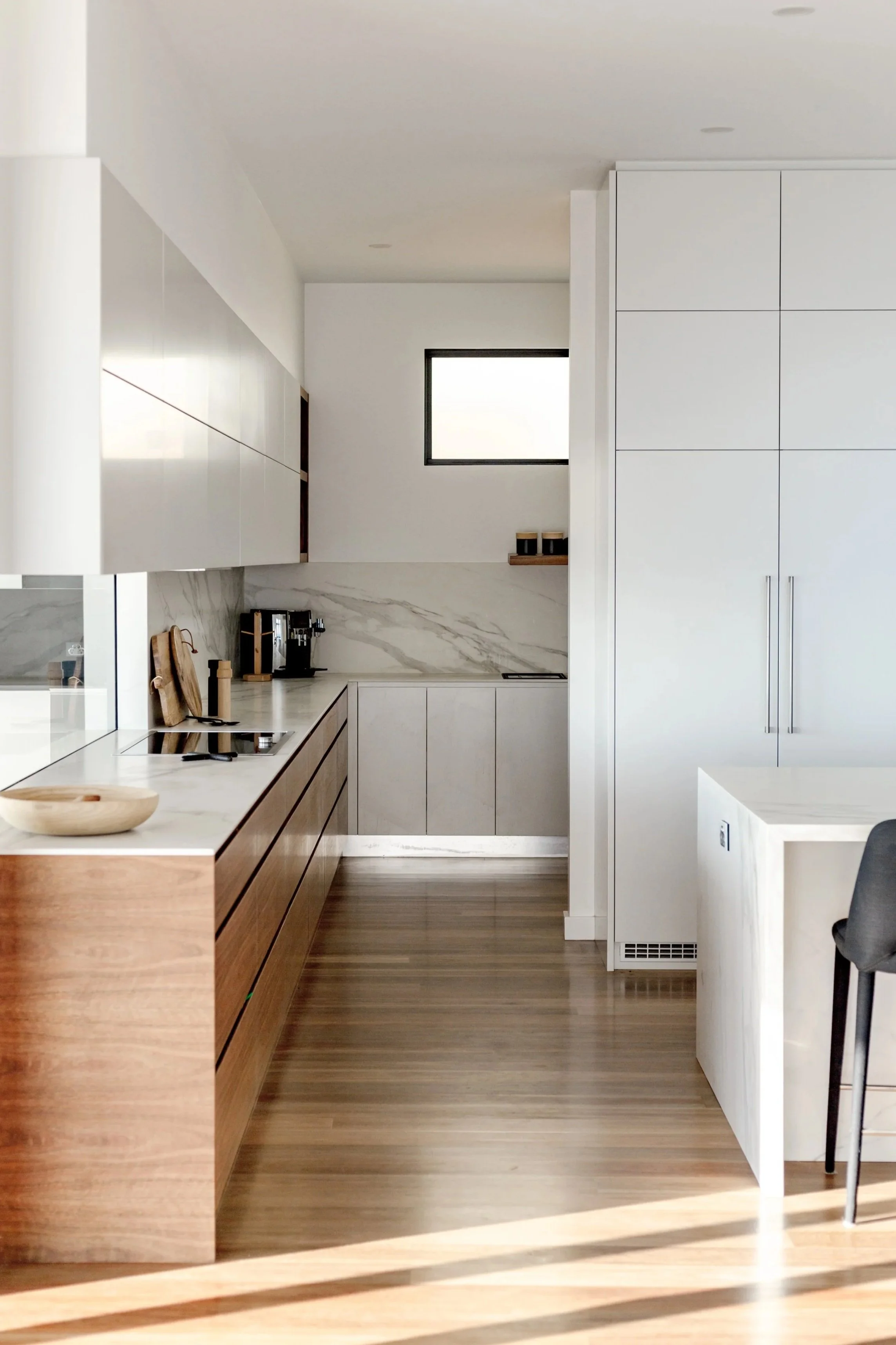 Gather Studio - Redhead Beach House. Modern kitchen with wood cabinetry, marble countertops, a small window near the ceiling, and minimal decor.