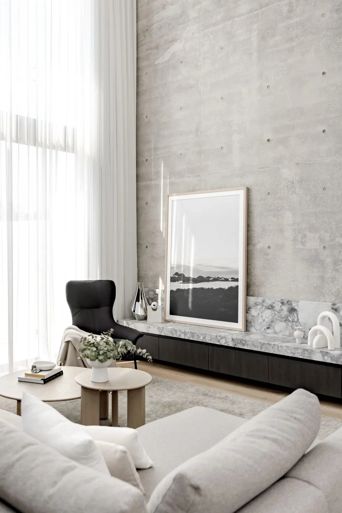 Gather Studio - Bar Beach Residence. Modern living room with light sofa, black accent chair, marble, large framed black and white landscape photo, decorative vases, and minimalistic decor, illuminated by natural light through sheer curtains.