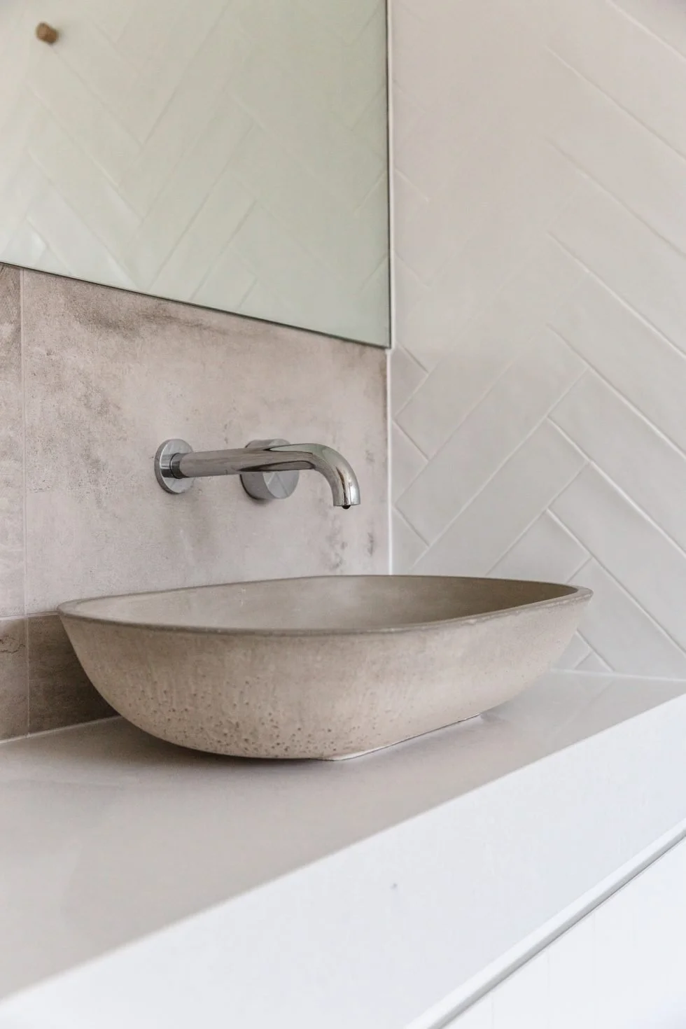 Gather Studio - Bay Residence Air bnb. A minimalist bathroom sink with a round, stone basin, a wall-mounted faucet, a mirror, and textured tile walls.