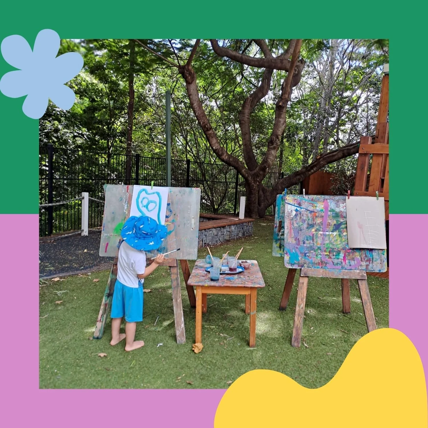 Child in white T-shirt and blue shorts, with a blue headscarf, painting outdoor on an easel in a yard with trees and fence, surrounded by art supplies and completed paintings.