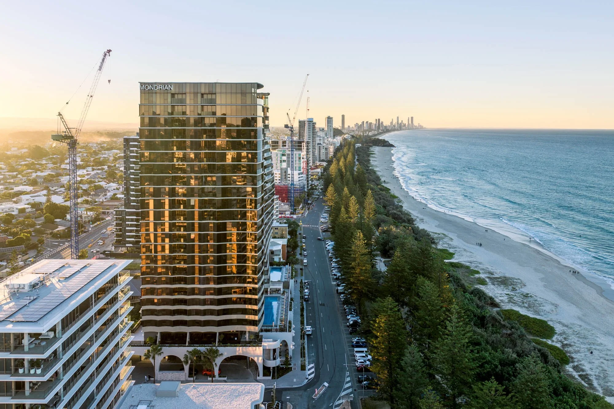 High-rise hotel building named Mondrian overlooking a beach with a city skyline in the background during sunset.