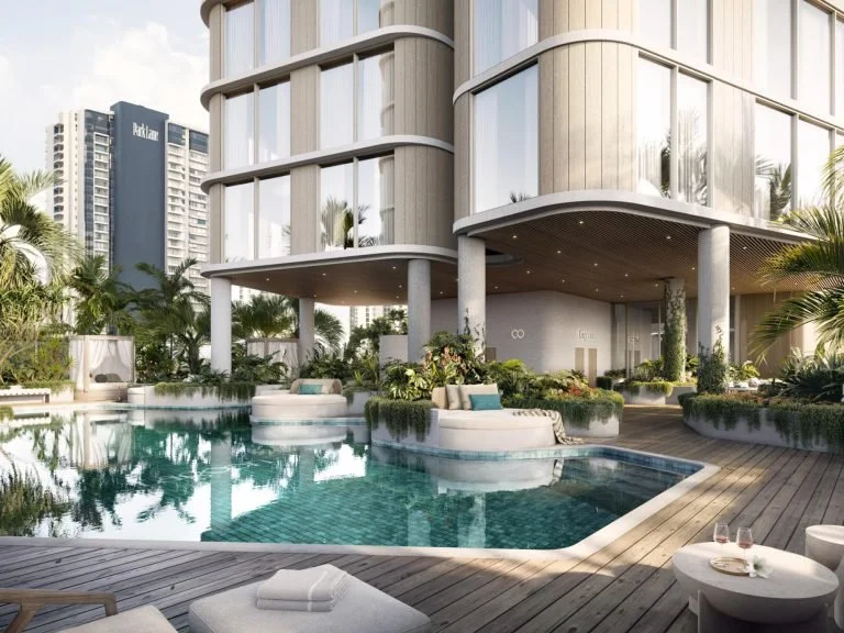 Luxury hotel pool area with lounge chairs, tropical plants, and a modern multi-story building in the background.