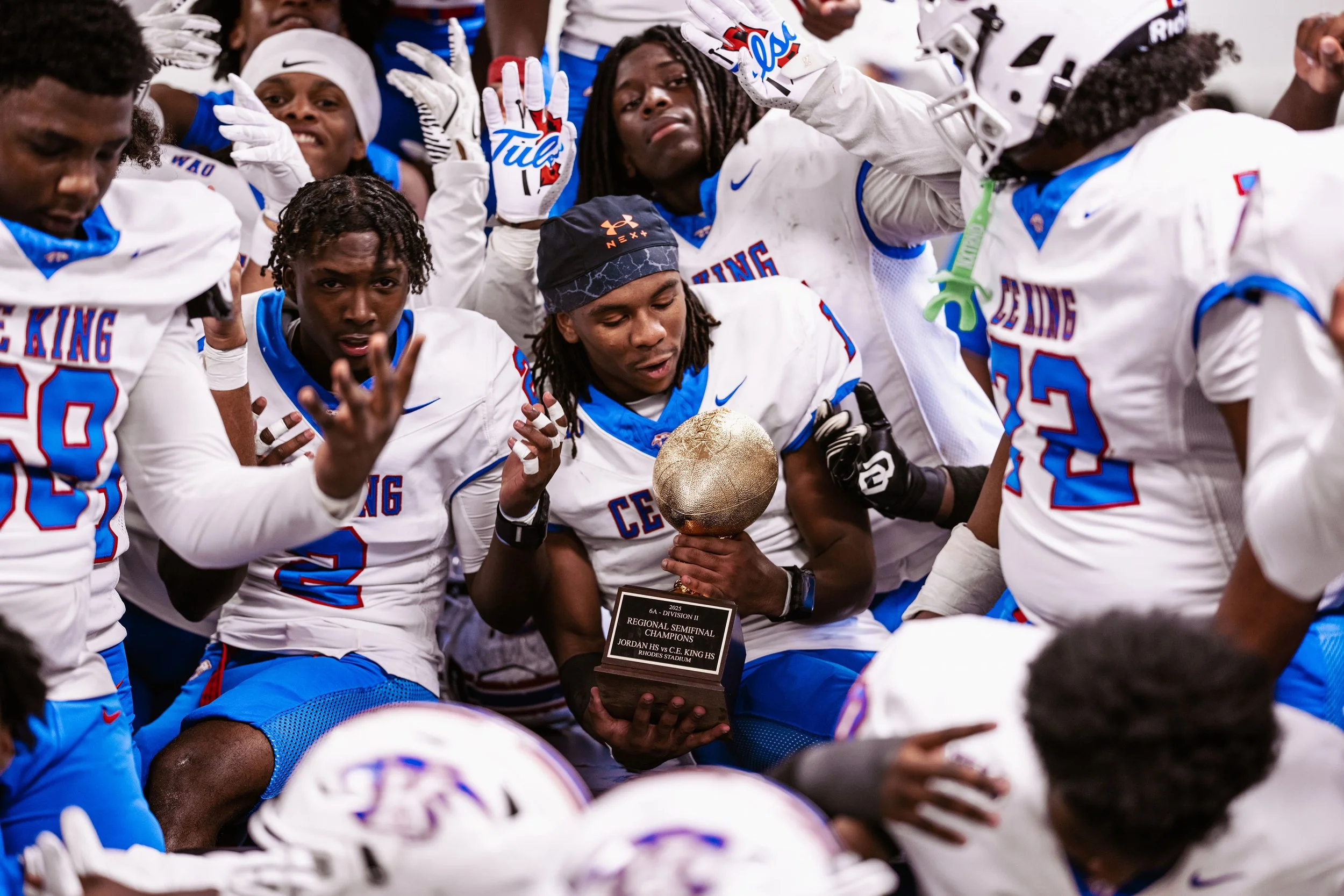 Football players in white and blue jerseys celebrating with a trophy after a victory.