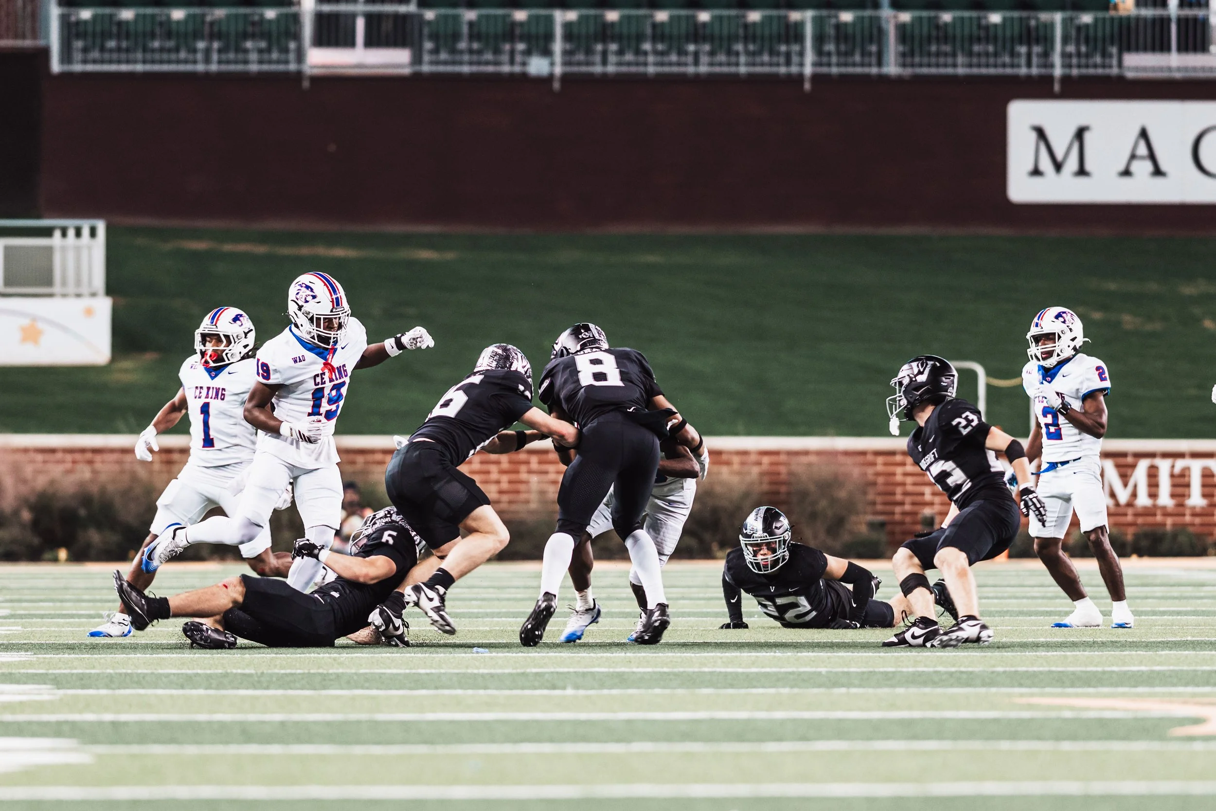 American football players in black and white uniforms on a field during a game, with some players tackling and others running with the ball.