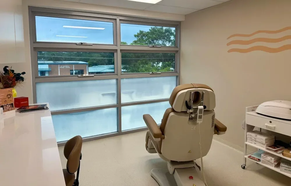 Treatment room at The Derm Clinic in Kingscliff, with an examination chair beside a window.