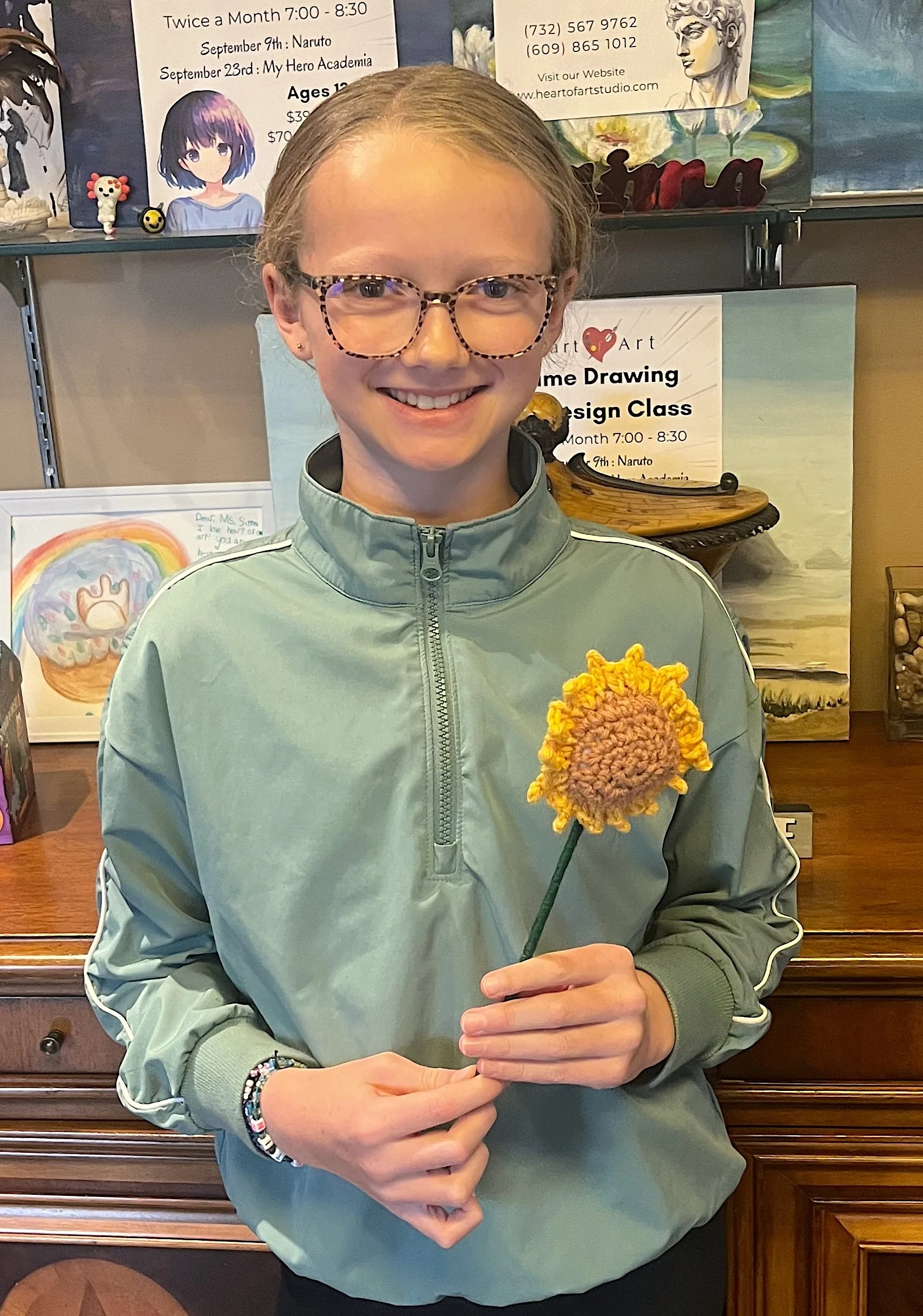 Student proudly holding a handmade crochet flower created in a kids crochet class at Heart of Art Studio