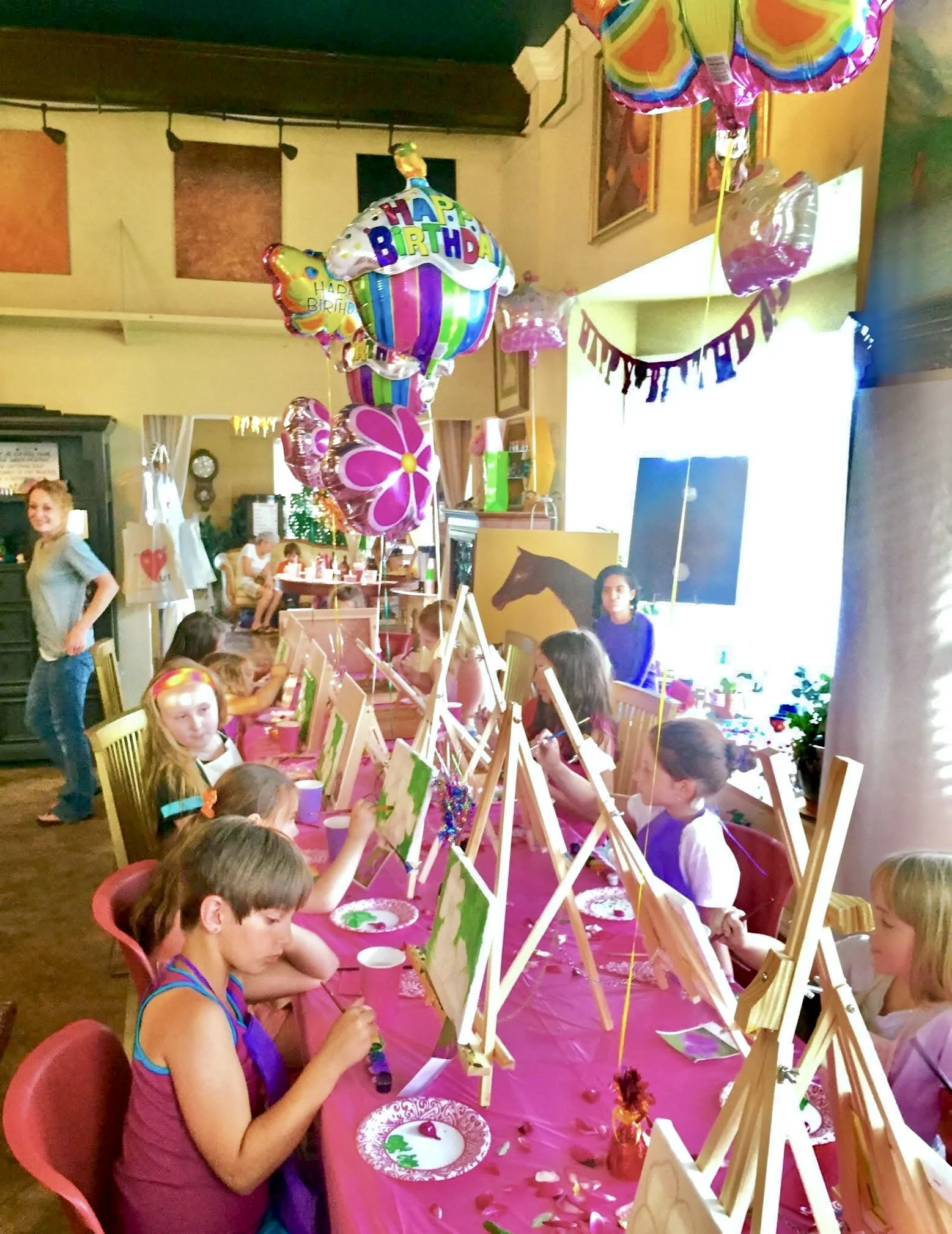 Kids painting in instructor led paint party with setup of easels, canvases, brushes and all painting supplies