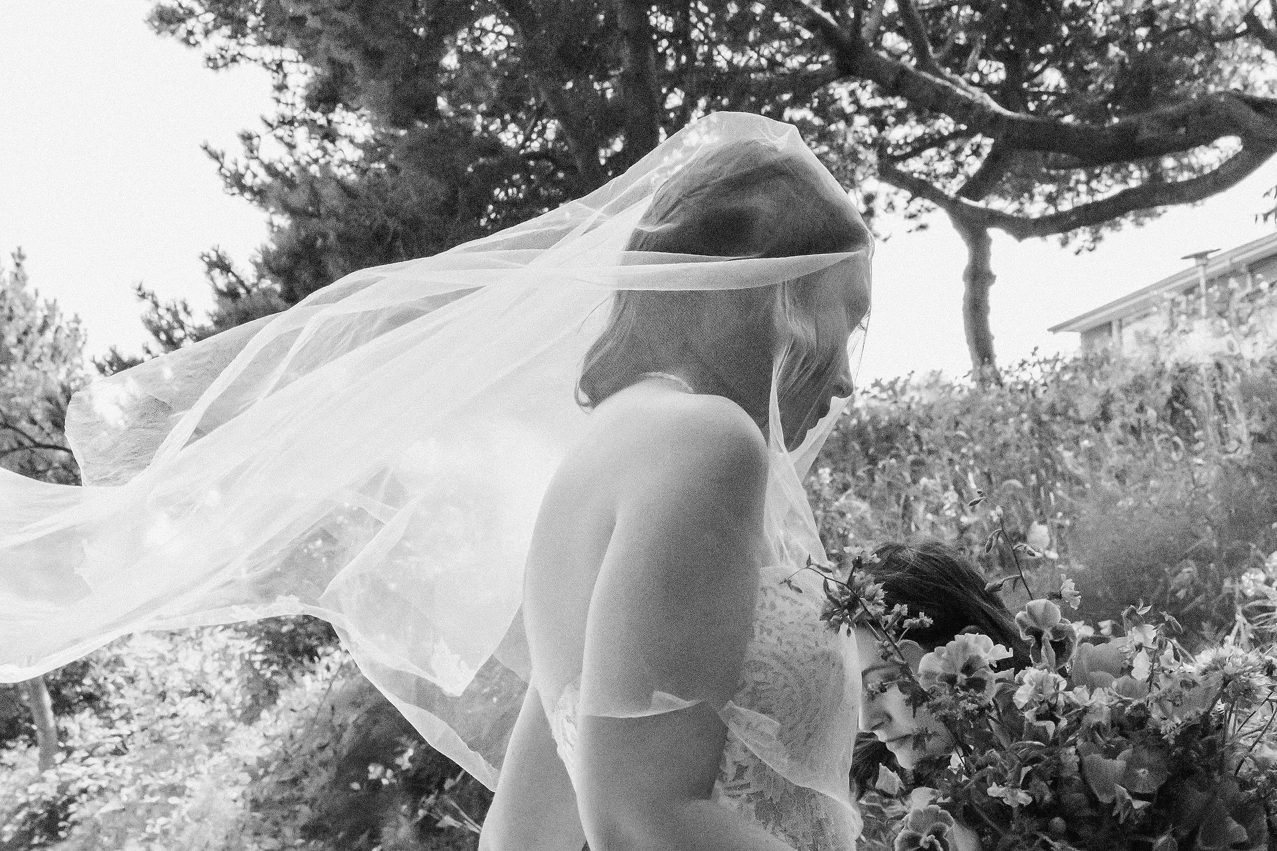 Beautiful bride stands underneath trees near a lake where she is about to get married outdoors and celebrate in the boathouse.