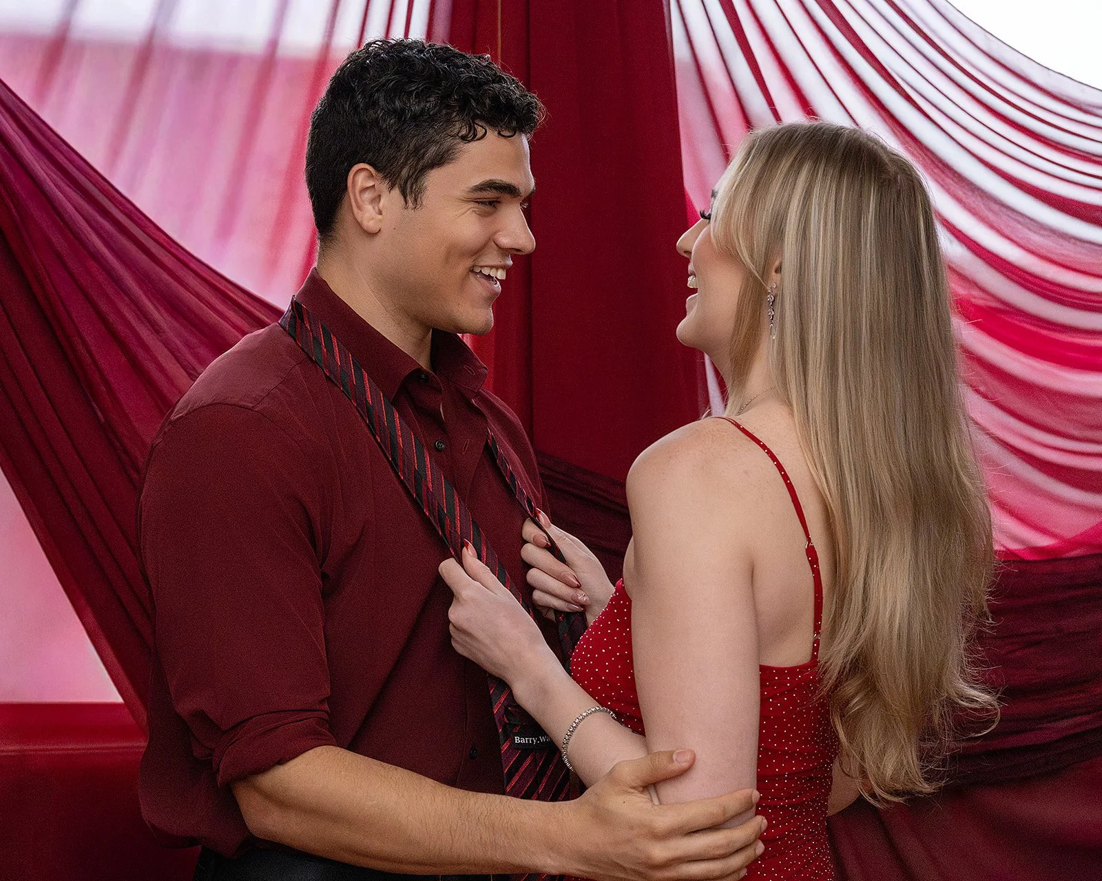 Couple in coordinated red outfits hold each other while laughing. Couples engagement photoshoots.