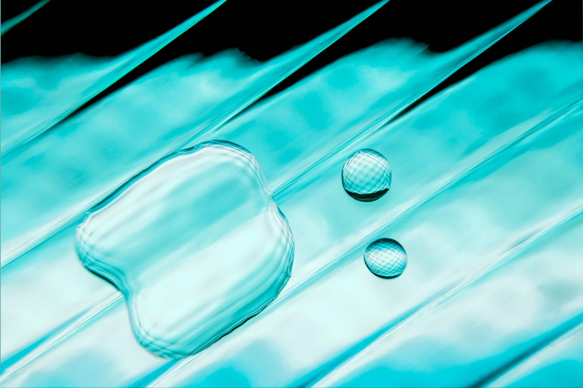 Abstract photograph titled Drop of Life by Nahid Naderi. Features luminous turquoise water droplets on a dark background, symbolizing the irreplaceable value and vital preservation of water.