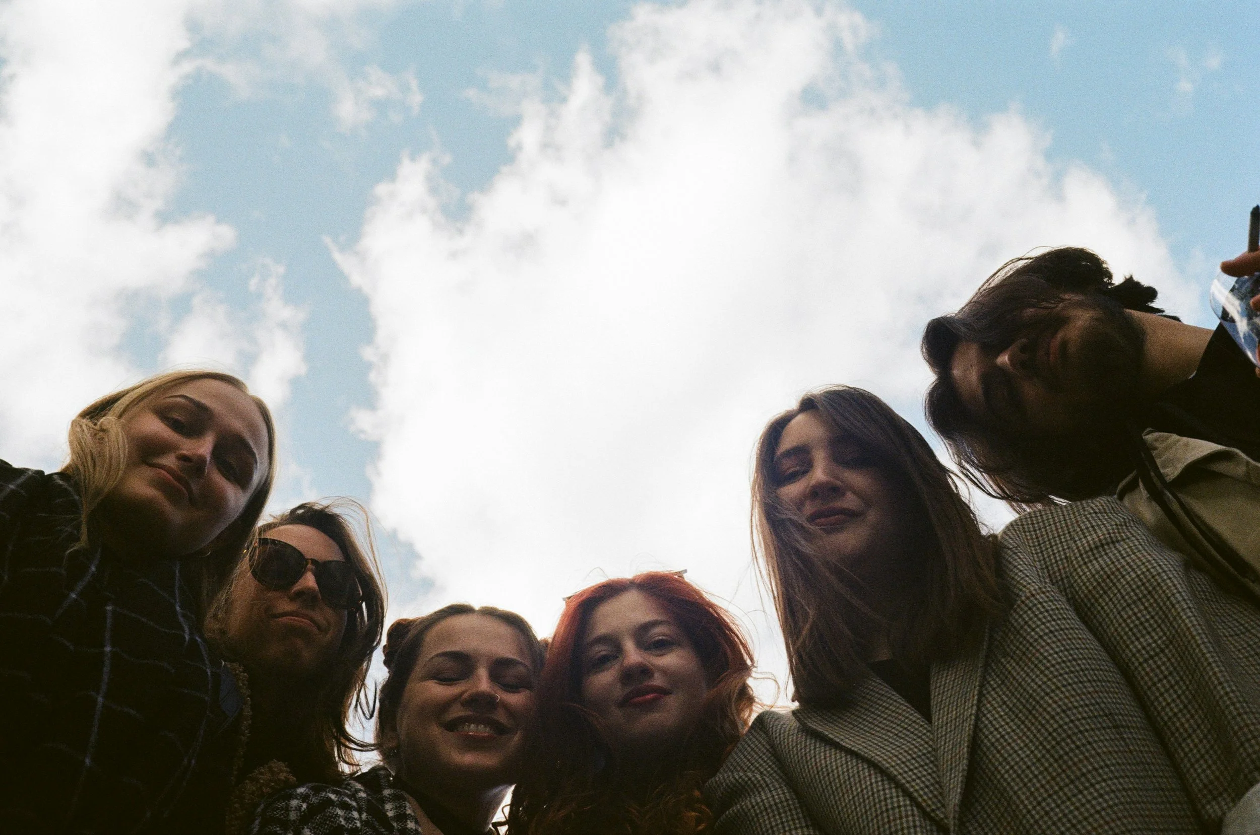 Group of six people looking down at the camera with a cloudy blue sky background.