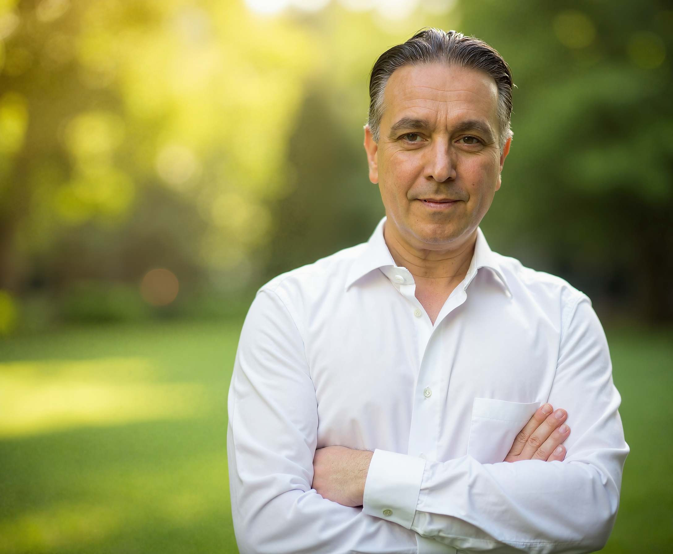 Mann in weißem Hemd mit verschränkten Armen im Grünen.