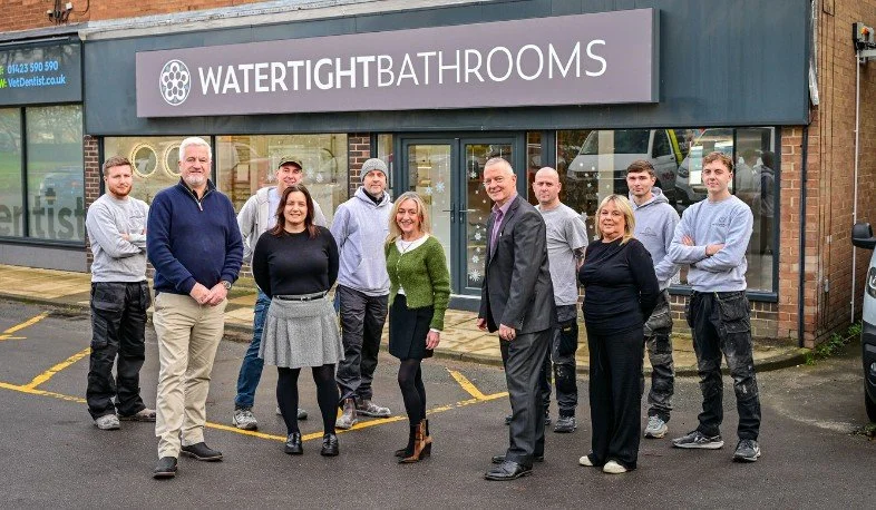 Group of ten people standing outside a bathroom store called 'Watertight Bathrooms,' smiling at the camera.