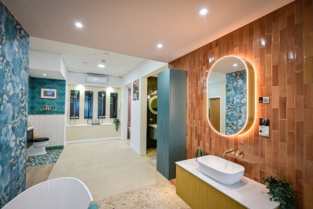 Modern bathroom with a wooden brick wall, illuminated mirror, vessel sink, and a blue partition. In the background, a shower area with multiple shower heads and a toilet.