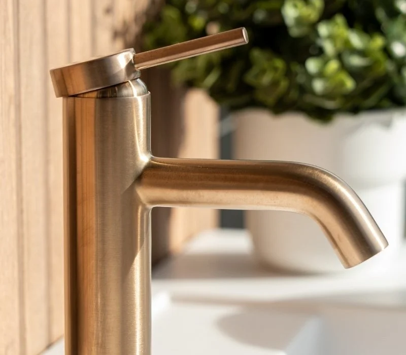 Stainless steel kitchen faucet with a brushed finish and a pull-up spout, set against a wooden backsplash and a potted plant in the background.