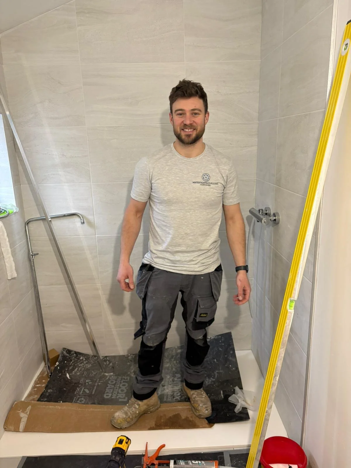 Smiling middle-aged man with short gray hair, wearing a colorful floral shirt and a maroon sweater, standing indoors near wooden stairs.