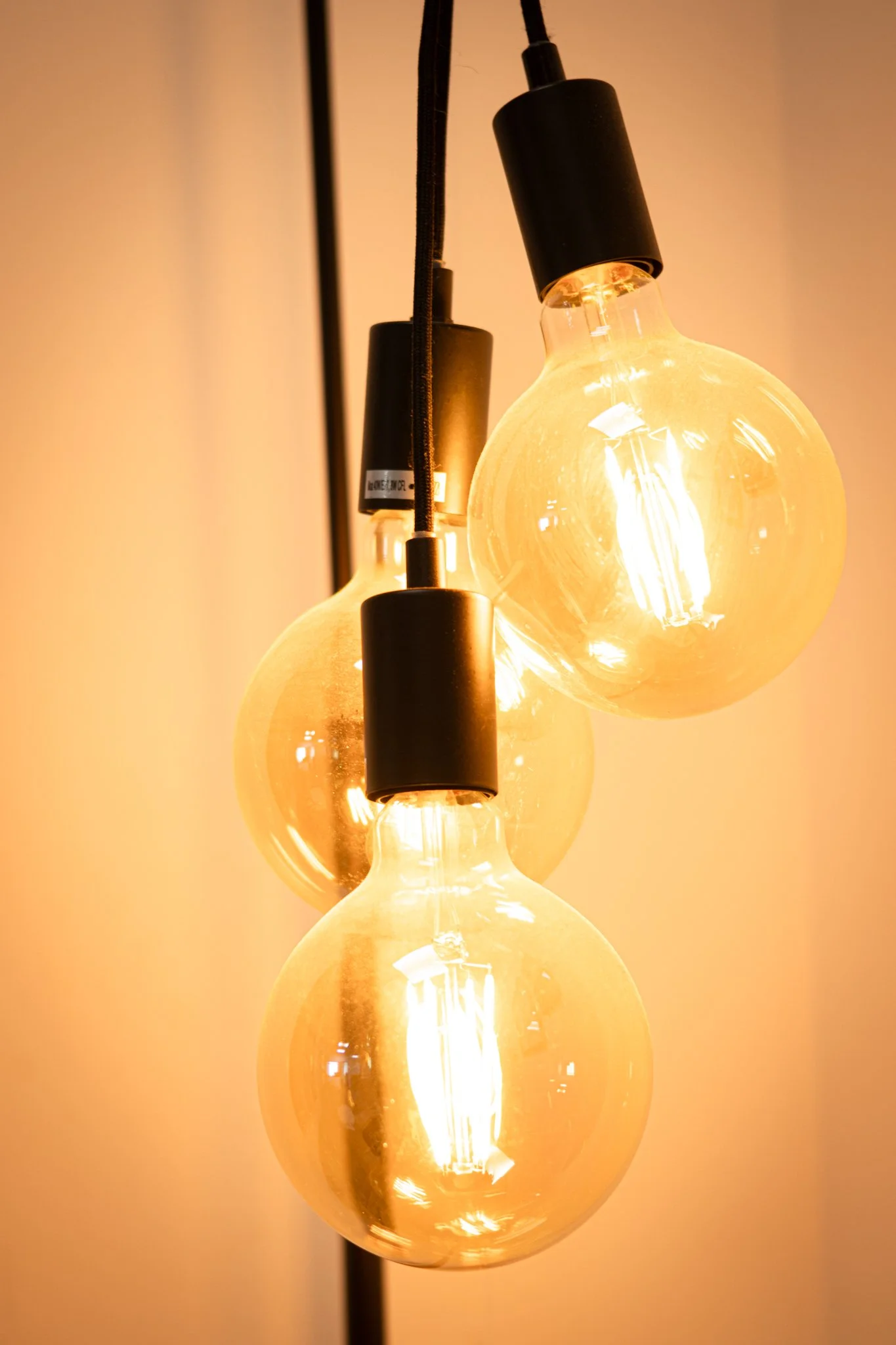 Three glowing vintage-style Edison light bulbs hanging from black sockets against a warm beige background.