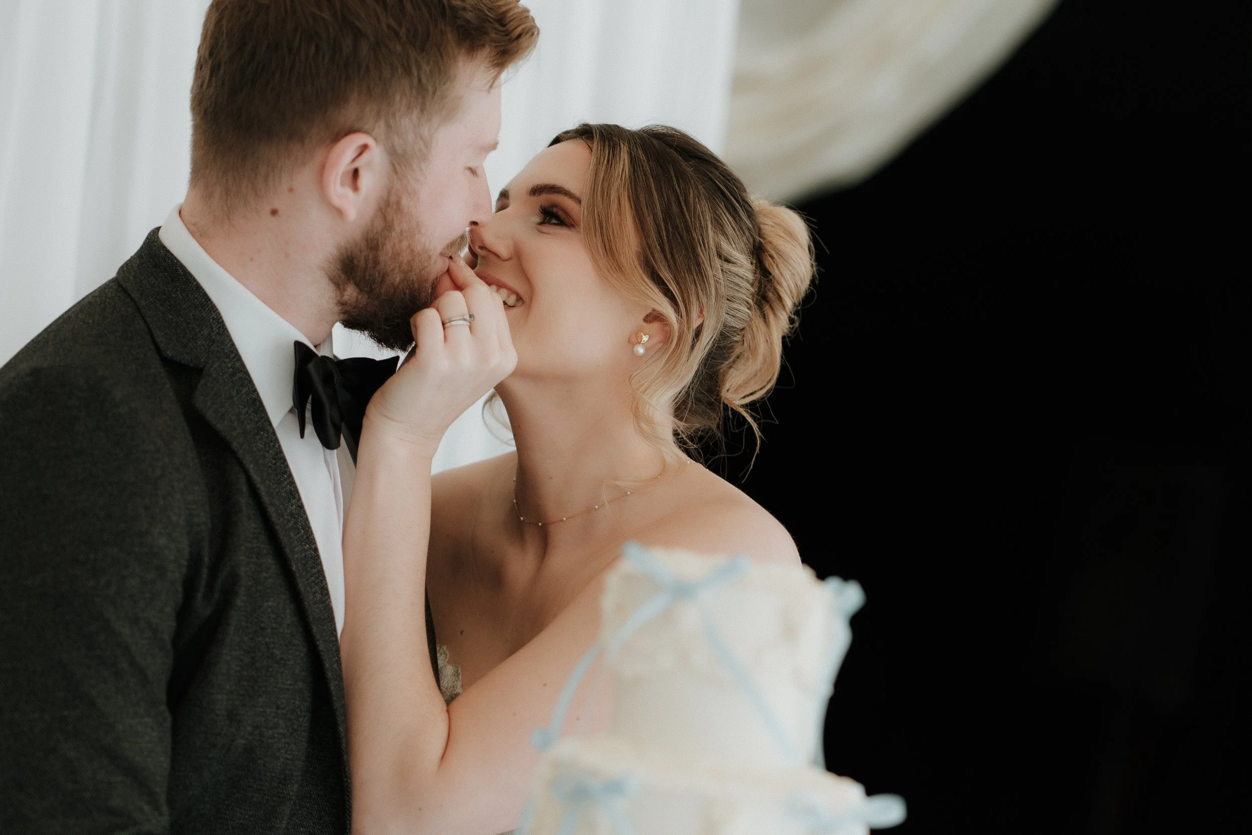 A bride and groom sharing a close, intimate moment during their wedding, with the bride smiling and touching the groom's face as they lean toward each other.