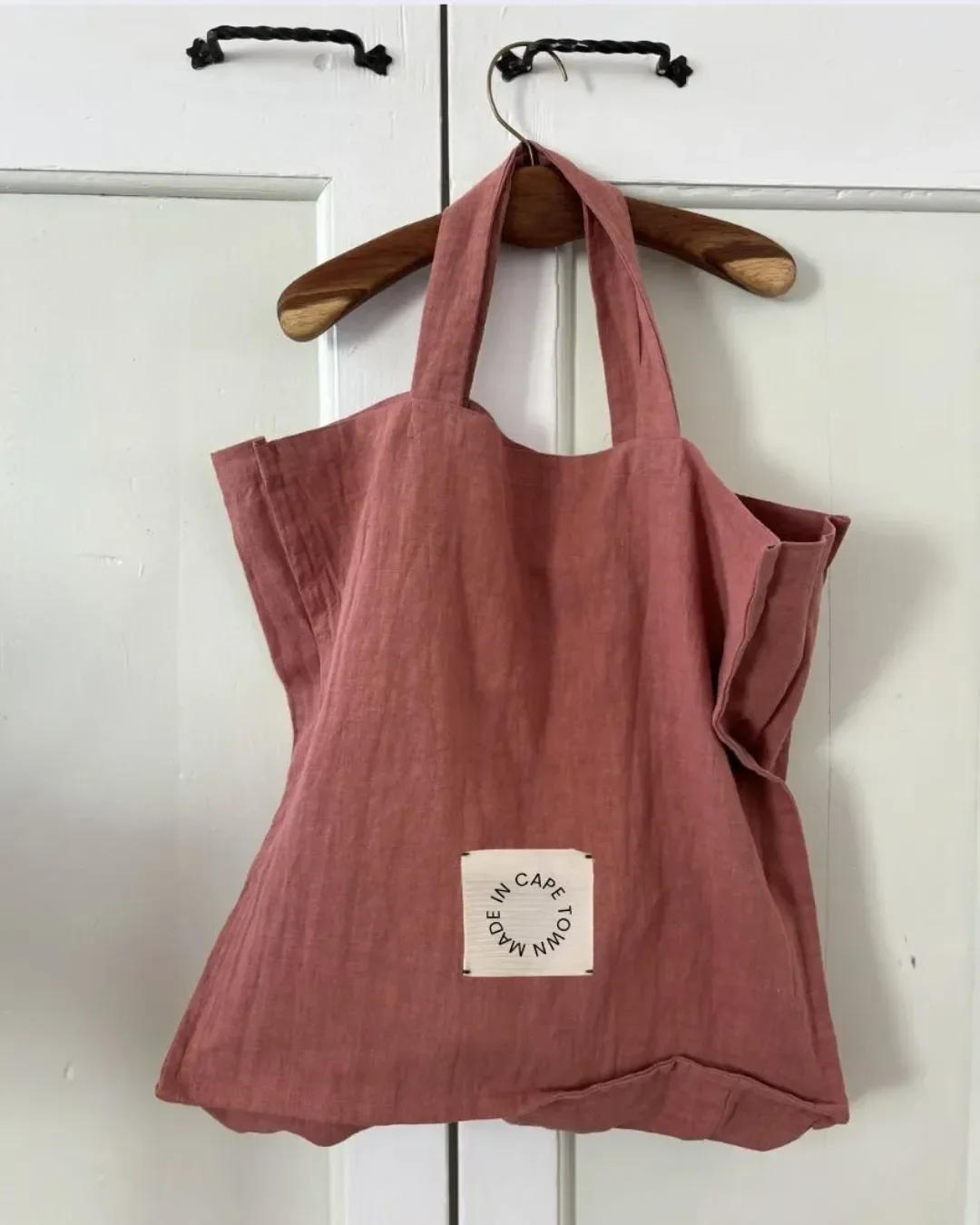 Rust-colored organic ramie Ember Tote bag hanging on a wooden hanger with a Made in Cape Town label, handmade by Soli in Cape Town.