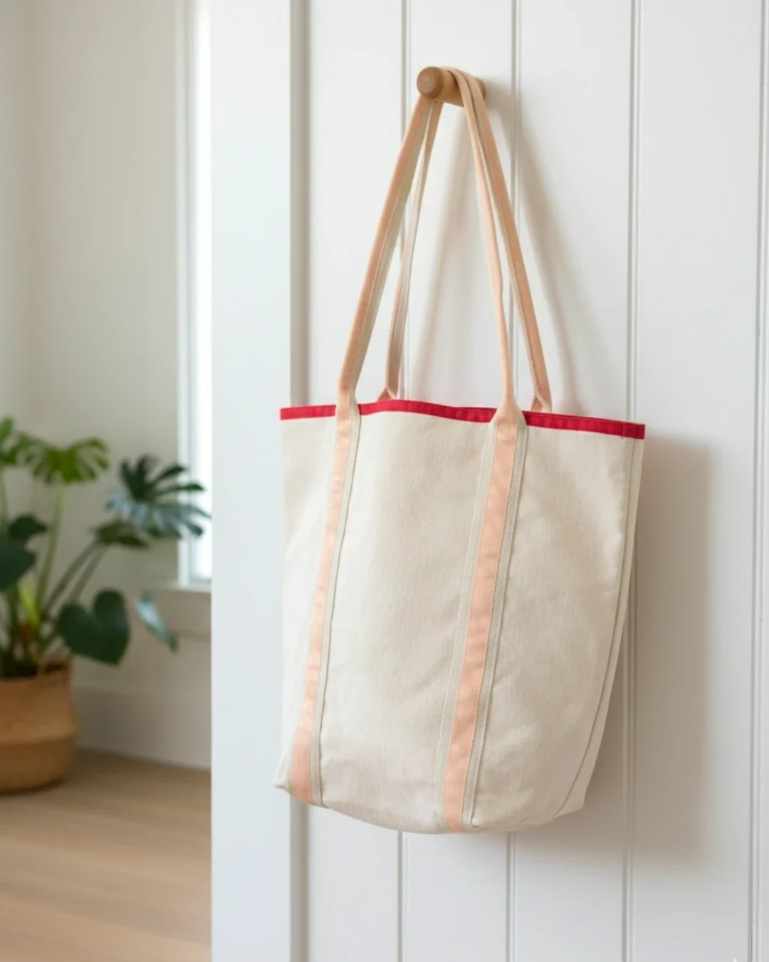 Cream heavy-weight cotton canvas Promenade bag hanging on a wooden peg, featuring peach-colored vertical straps and a red top trim, handmade by Soli in Cape Town for sustainable merchandise or corporate gifts.
