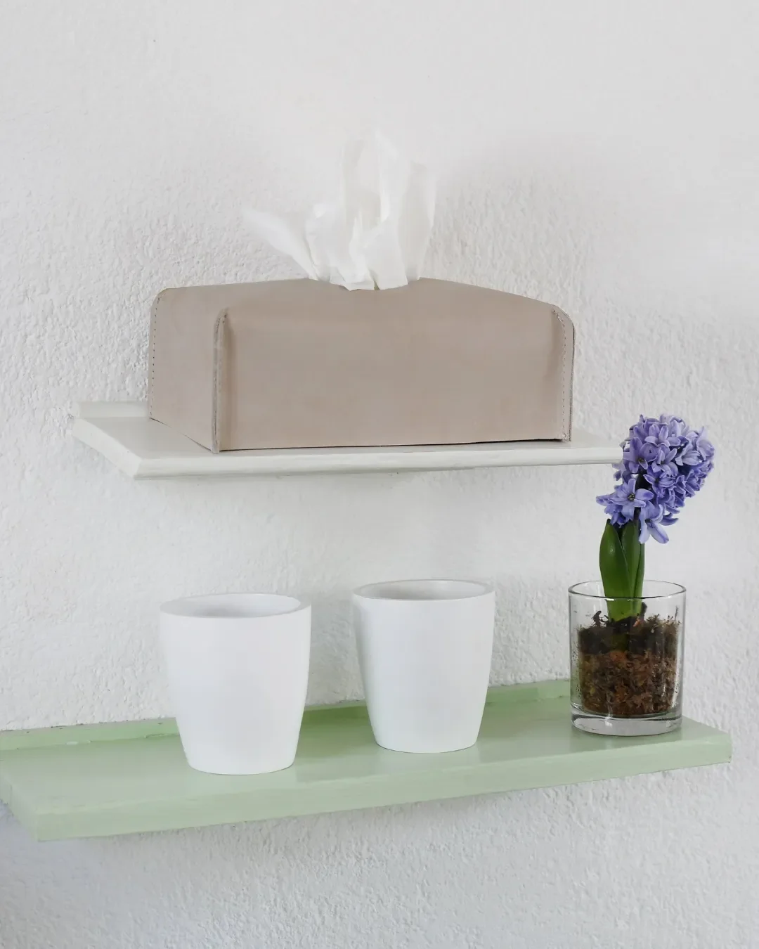 Handmade rectangular leather tissue box cover in a neutral stone color, displayed on a minimalist white shelf for luxury hotel room styling. By Soli, Made in Cape Town.