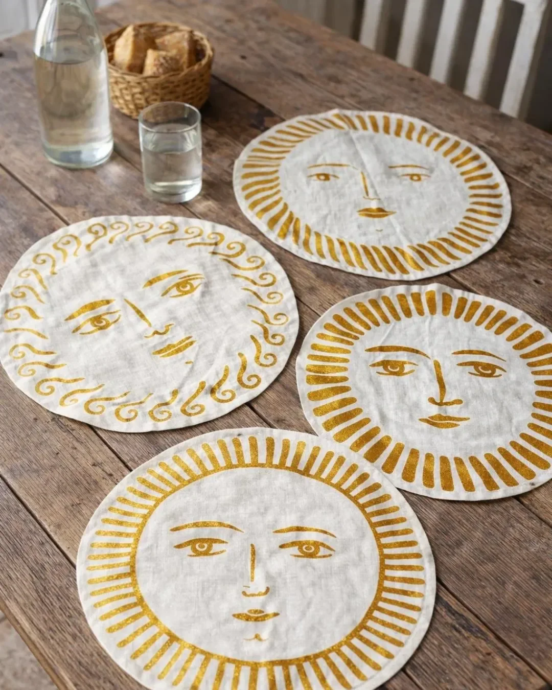 Four circular off-cream ramie placemats featuring gold sun face illustrations on a wooden dining table, handmade by Soli in Cape Town for sustainable merchandise or corporate gifts.