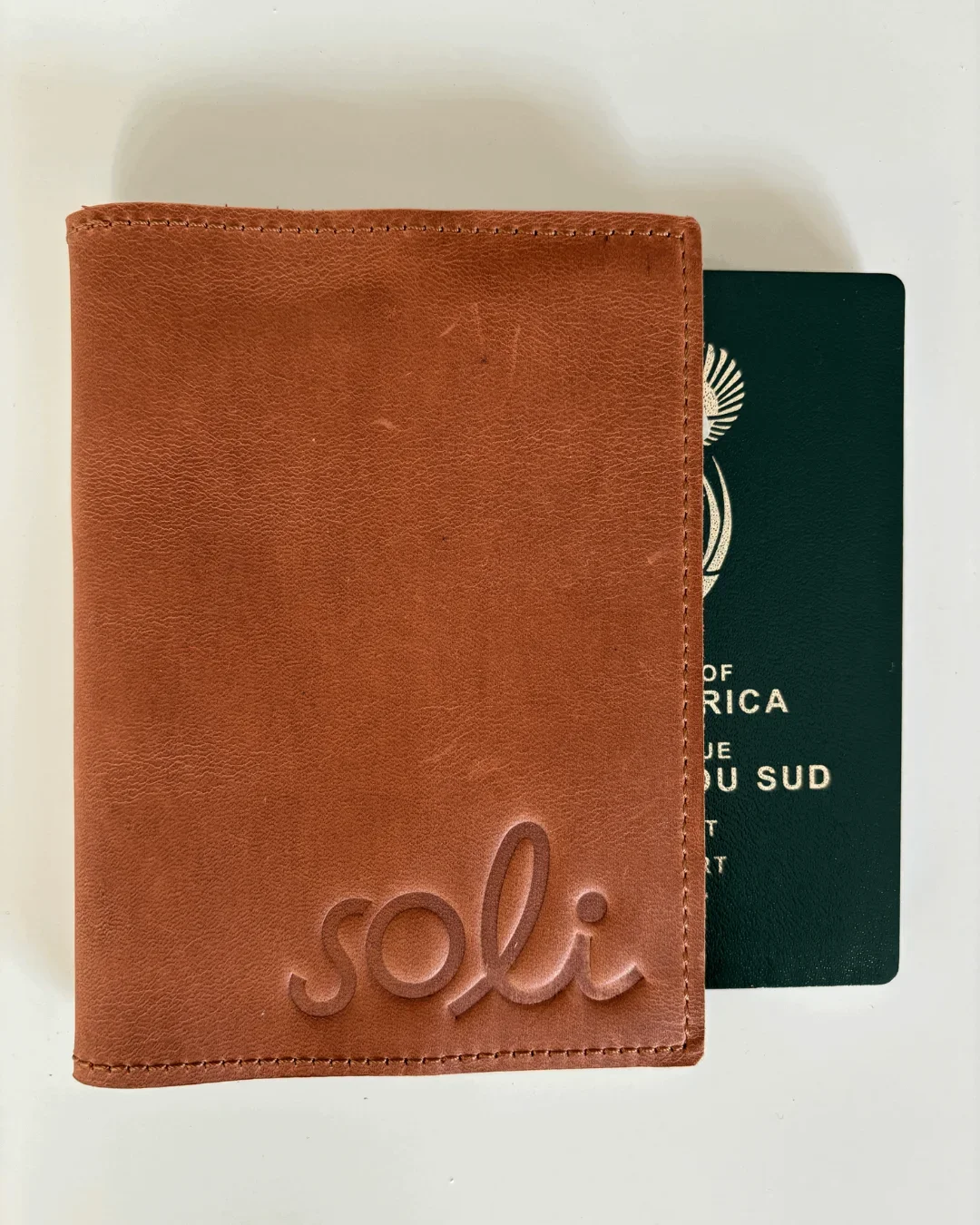 A genuine tan leather passport holder featuring a debossed "Soli" logo alongside a South African passport, Handmade by Soli in Cape Town for sustainable merchandise or corporate gifts.