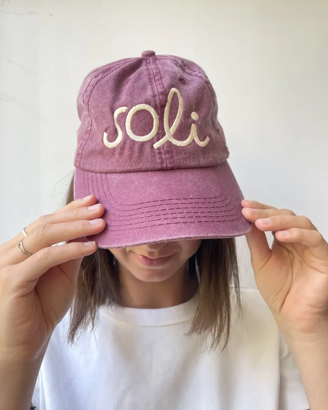 A person wearing a vintage-style washed plum cotton cap featuring the "Soli" logo in cream-colored thick embroidery, customized as a sustainable corporate gift.