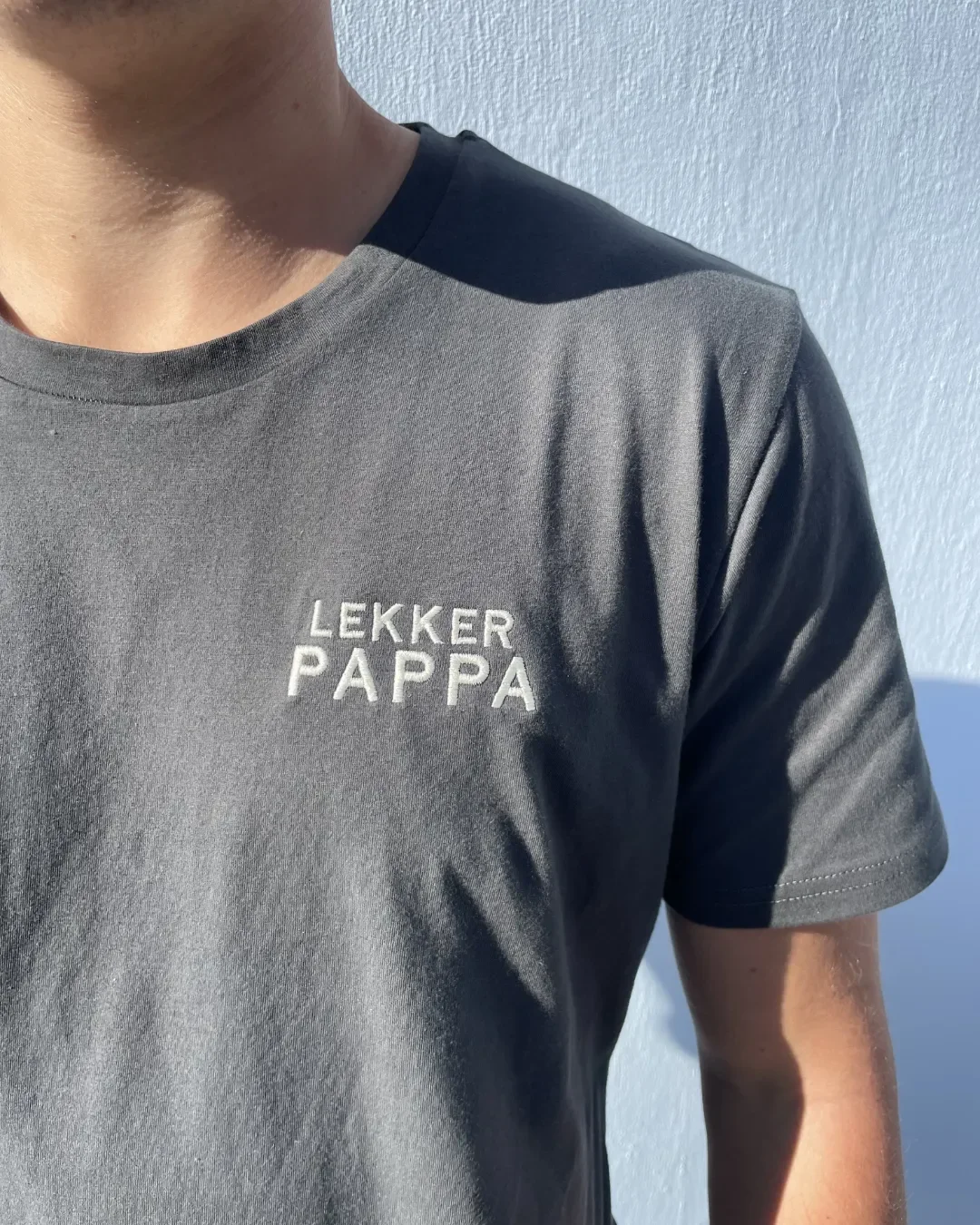 A man wearing a premium charcoal 100% cotton t-shirt with white "LEKKER PAPPA" embroidery, handmade by Soli in Cape Town for sustainable corporate gifting.