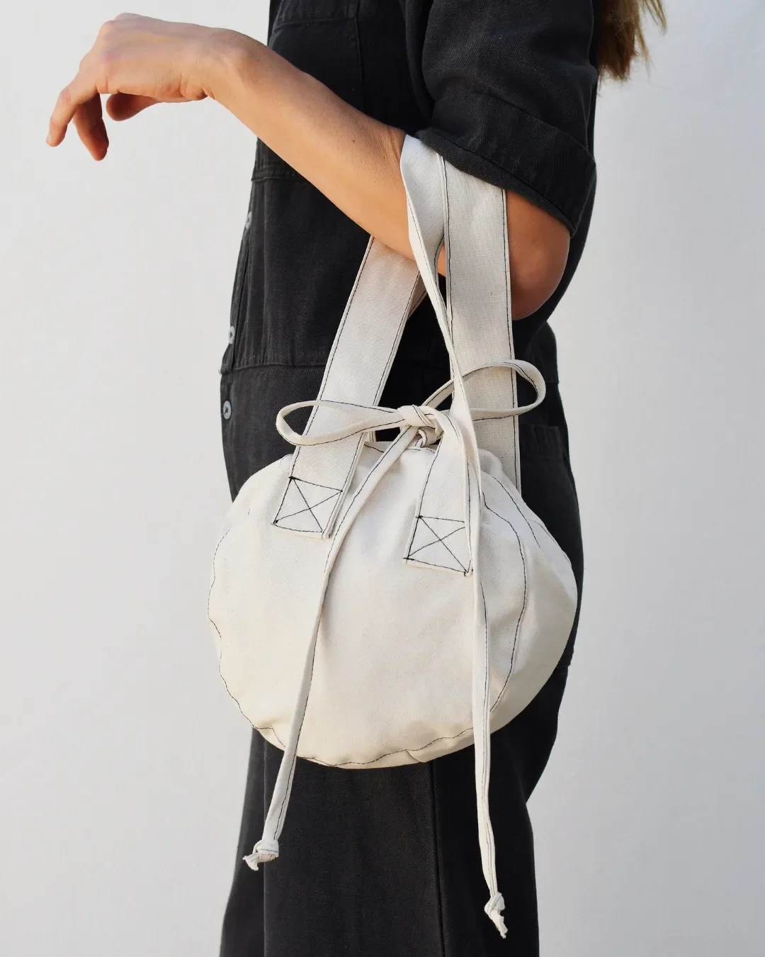 The small London Bag, a 22cm circular natural heavy canvas handbag with drawstring ties and black contrast stitching, Handmade by Soli in Cape Town for sustainable merchandise or corporate gifts.