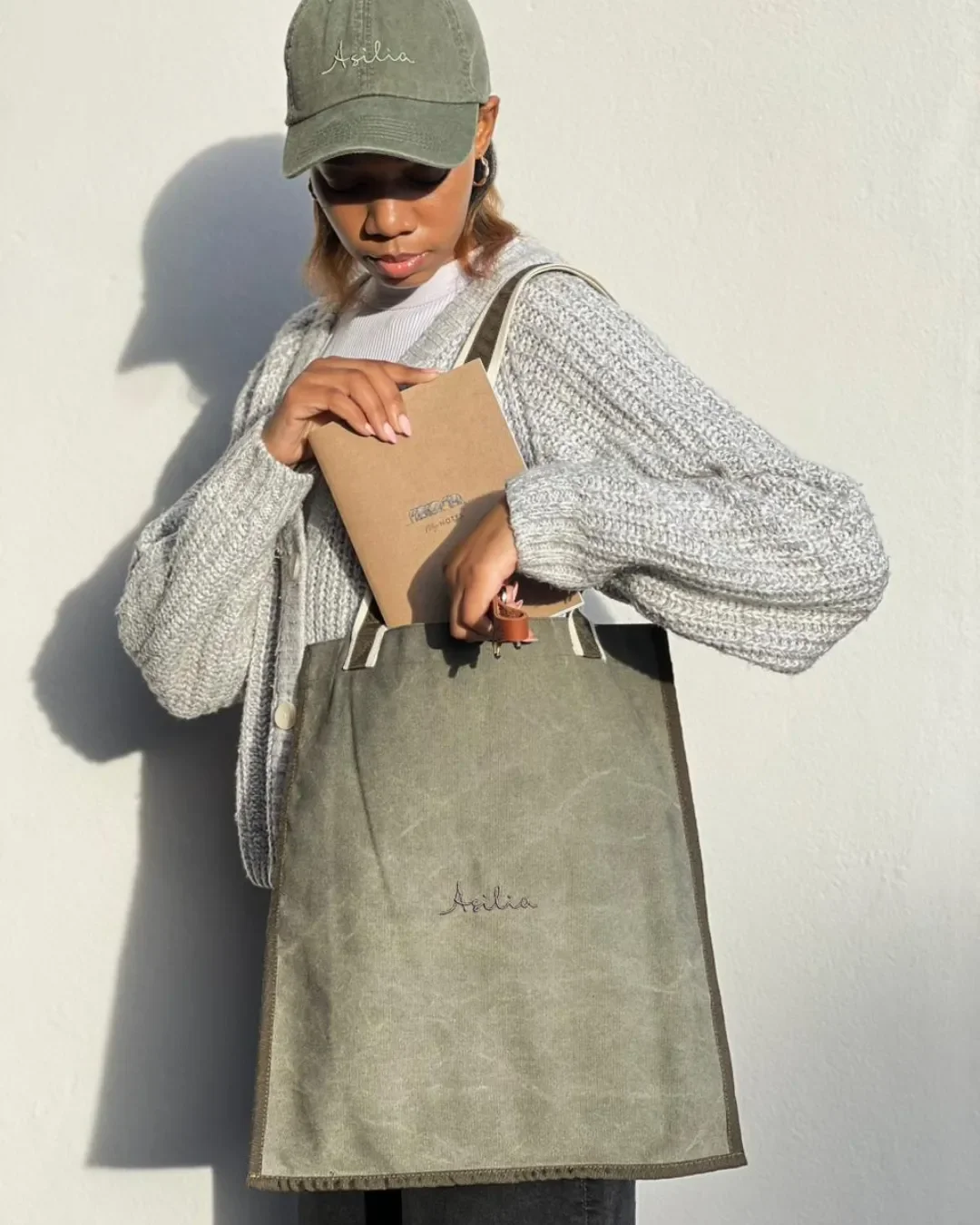 Woman wearing a branded Asilia cap holding a custom sustainable corporate gift tote bag in olive green, handmade by Soli in Cape Town for Asilia.