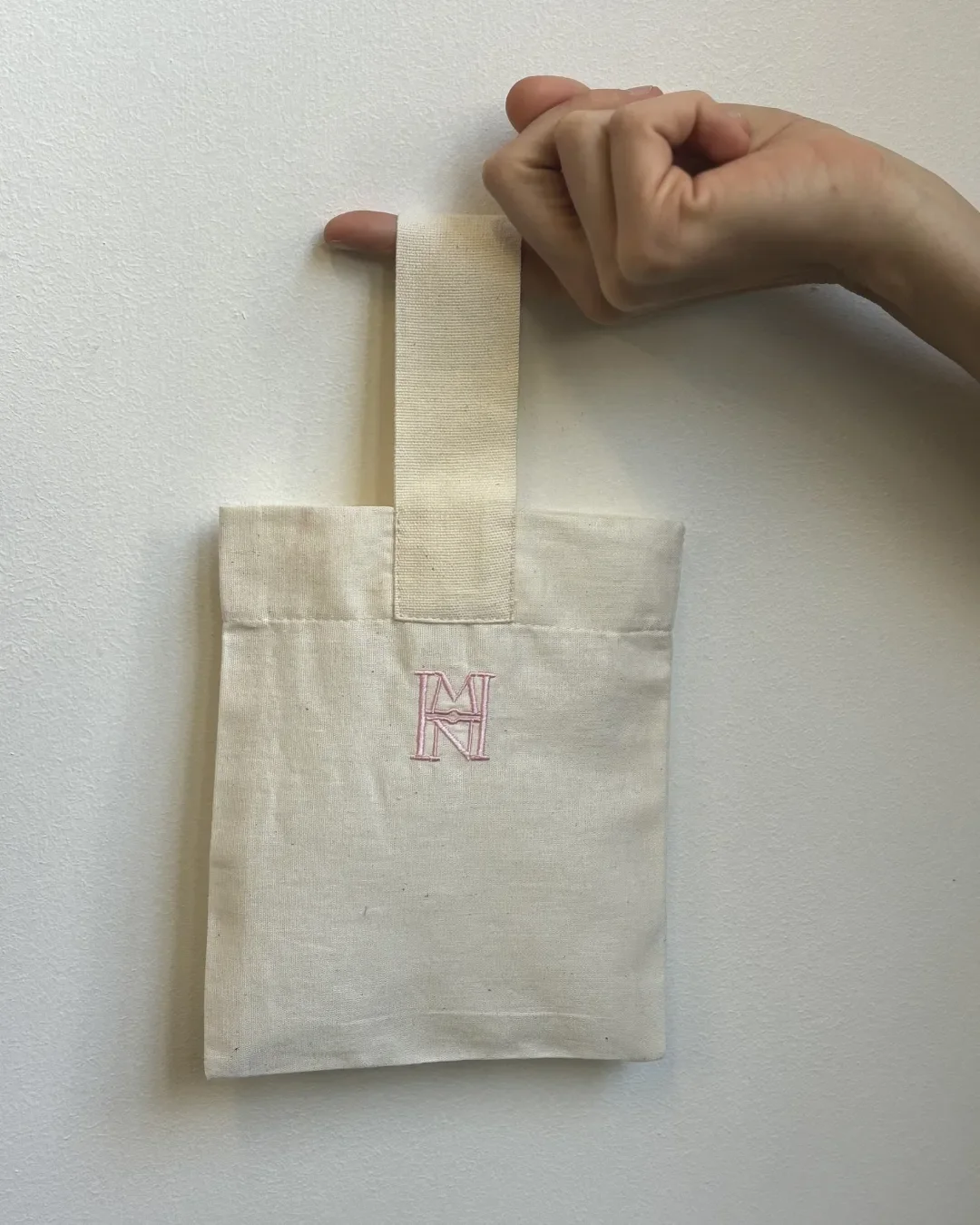 The small Mount Nelson Gift Bag in light natural calico fabric with a pink embroidered MN logo held against a white background, Handmade by Soli in Cape Town for sustainable merchandise or corporate gifts