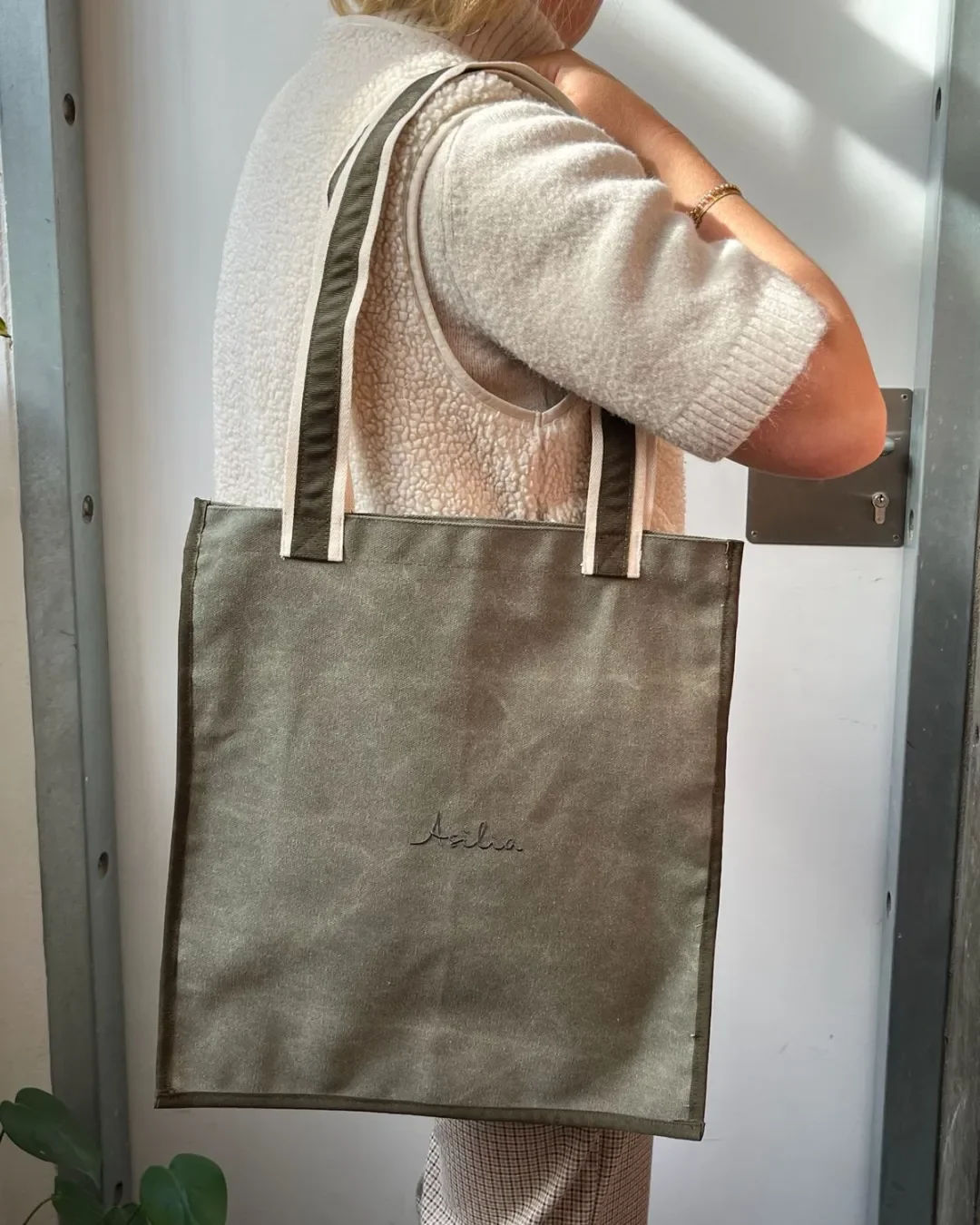 Side view of a person over-the-shoulder carrying a handmade olive green tote bag, custom sustainable corporate merchandise by Soli in Cape Town.