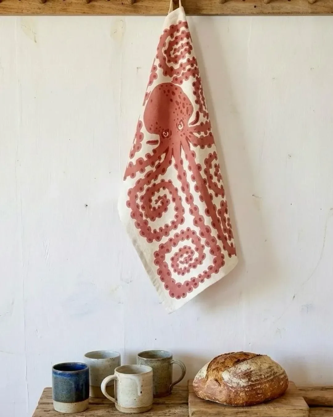 Extra large off-cream ramie tea towel featuring a rust-colored octopus print hanging in a rustic kitchen, handmade by Soli in Cape Town for sustainable merchandise or corporate gifts.