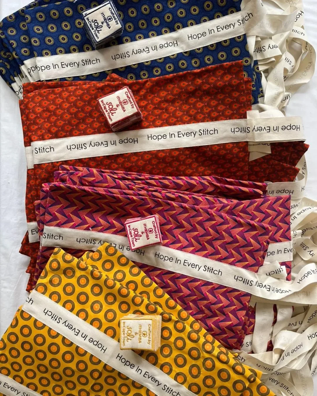 Authentic South African shweshwe tote bags with custom "Hope In Every Stitch" cotton ribbons, handmade by Soli in Cape Town for sustainable merchandise or corporate gifts.
