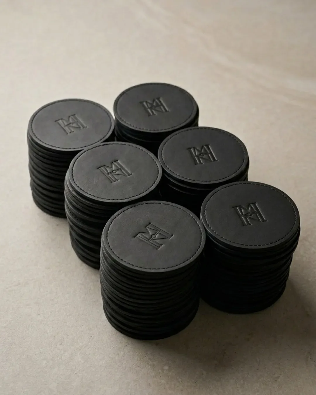 Stacked sets of handmade black leather coasters featuring a debossed custom logo, handcrafted by local artisans in Cape Town for sustainable corporate gifting and hospitality amenities.