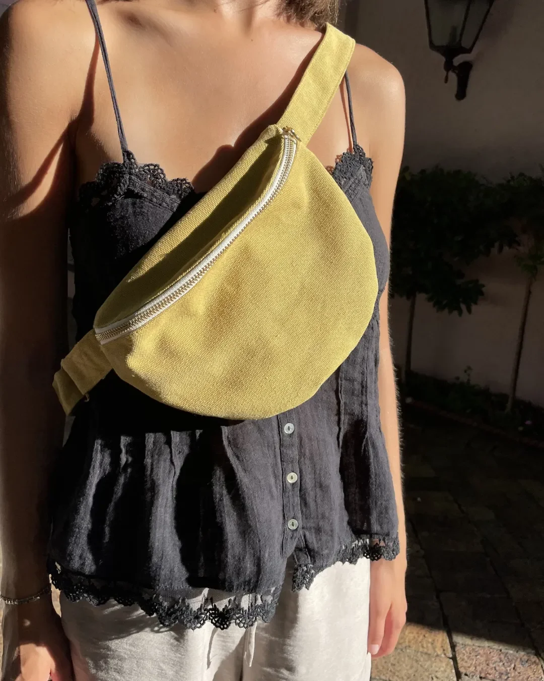 A person wearing a mustard yellow handmade cotton canvas moon bag with a silver zipper across a black lace-trimmed top, highlighting sustainable local craftsmanship from Cape Town by Soli for corporate gifts and merchandise.